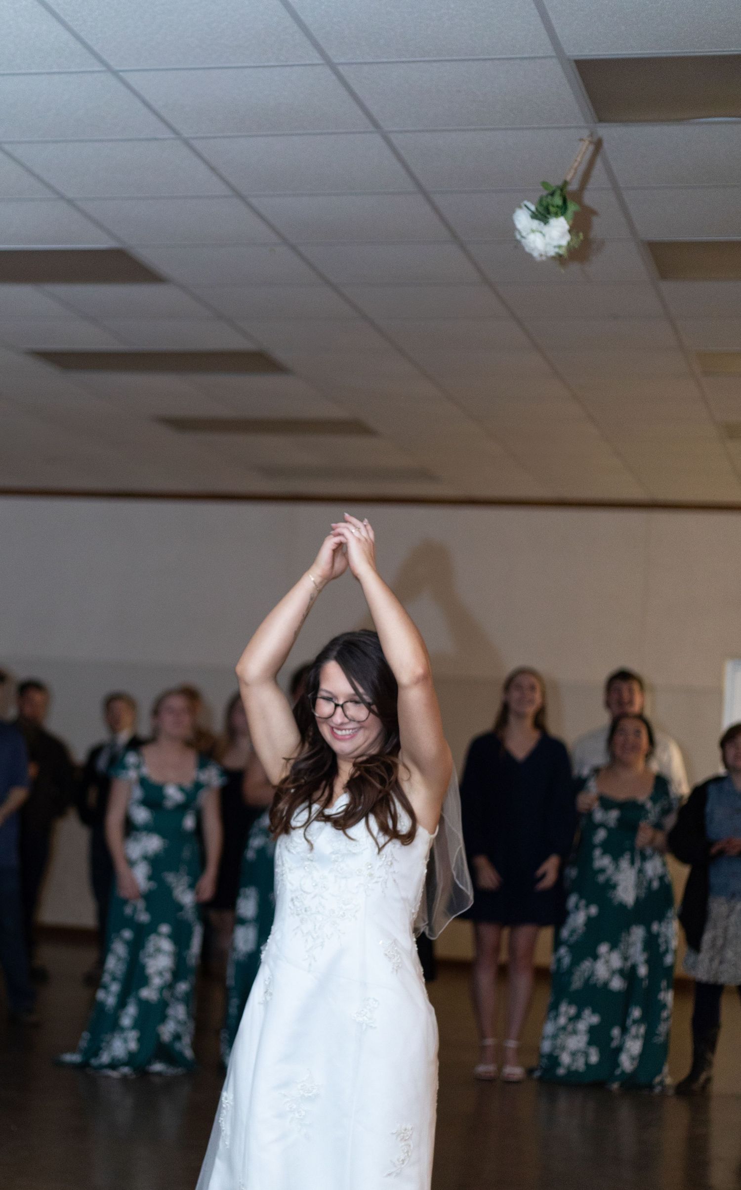 A bouquet being tossed at a wedding reception as guests in matching teal dresses watch with anticipation.