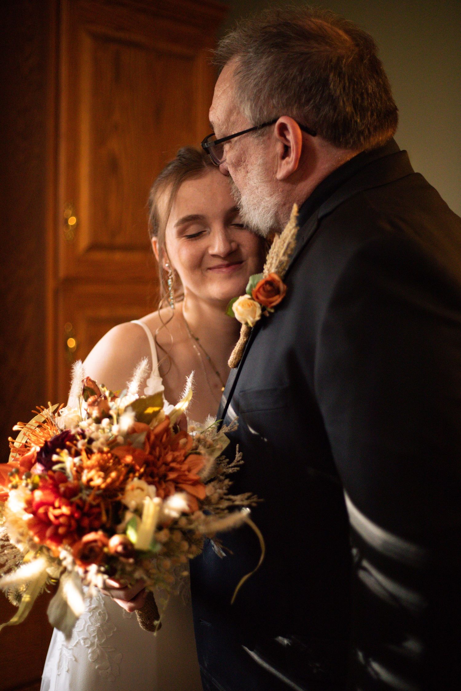 Romantic wedding couple shares tender moments in candlelit room with autumn-colored floral bouquet.