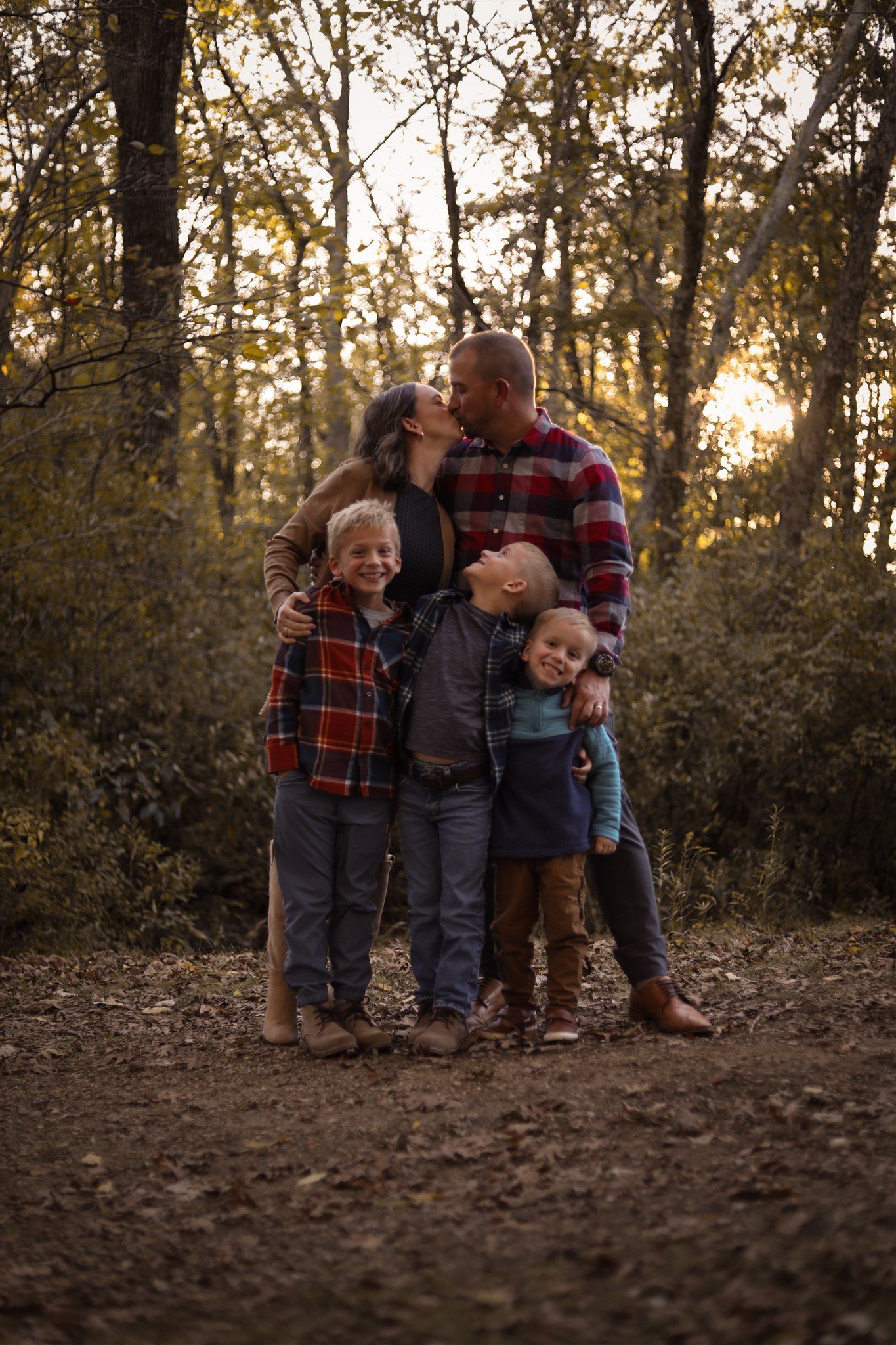 Family group poses together on forest path during sunset with golden backlighting.