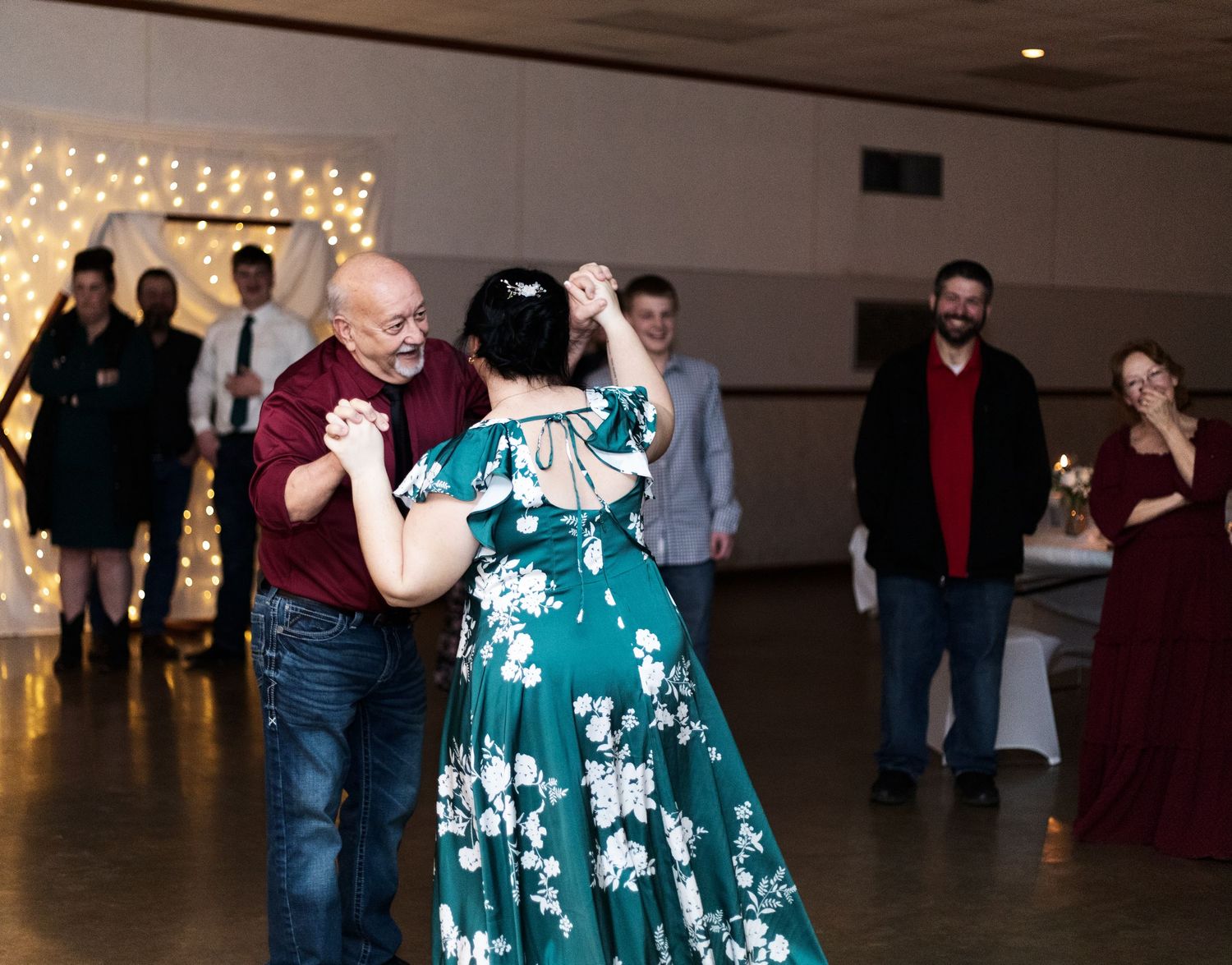 A group of people dancing at an indoor reception with string lights decorating the walls.