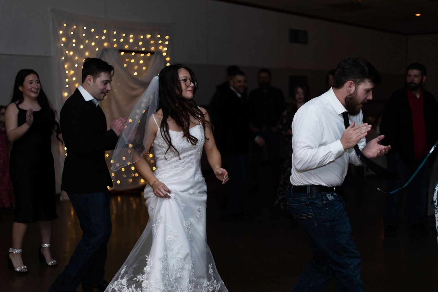 A couple shares a romantic dance together at a wedding reception with string lights glowing in the background.
