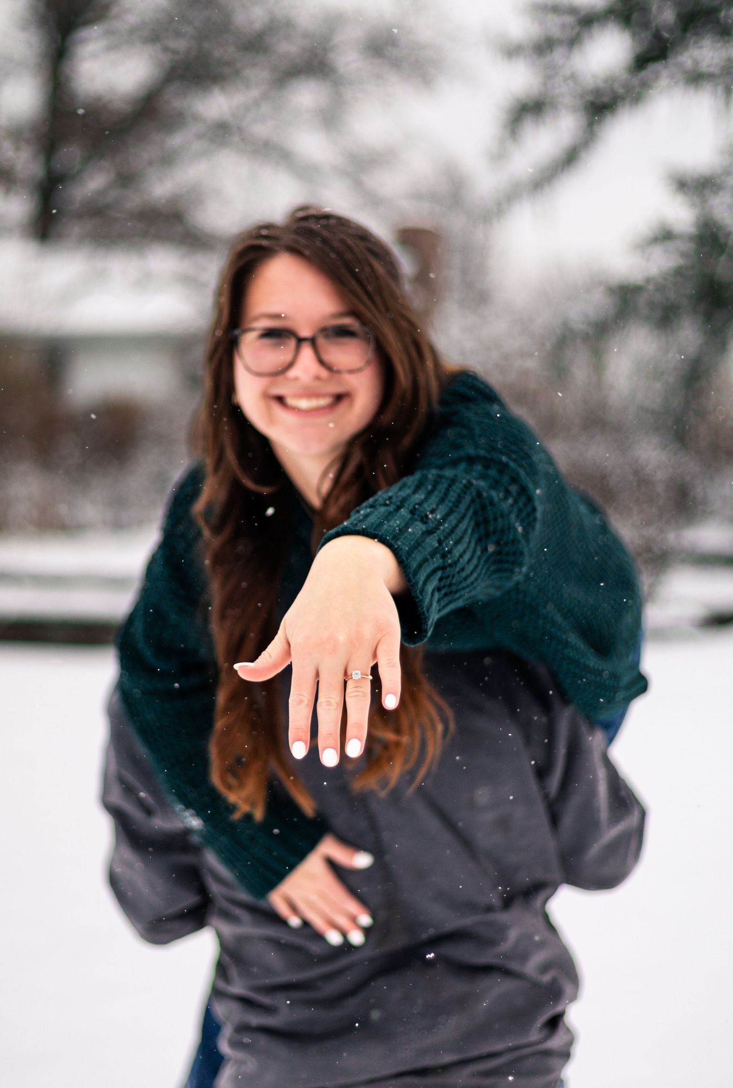 Someone shows off an engagement ring in a snowy winter setting.