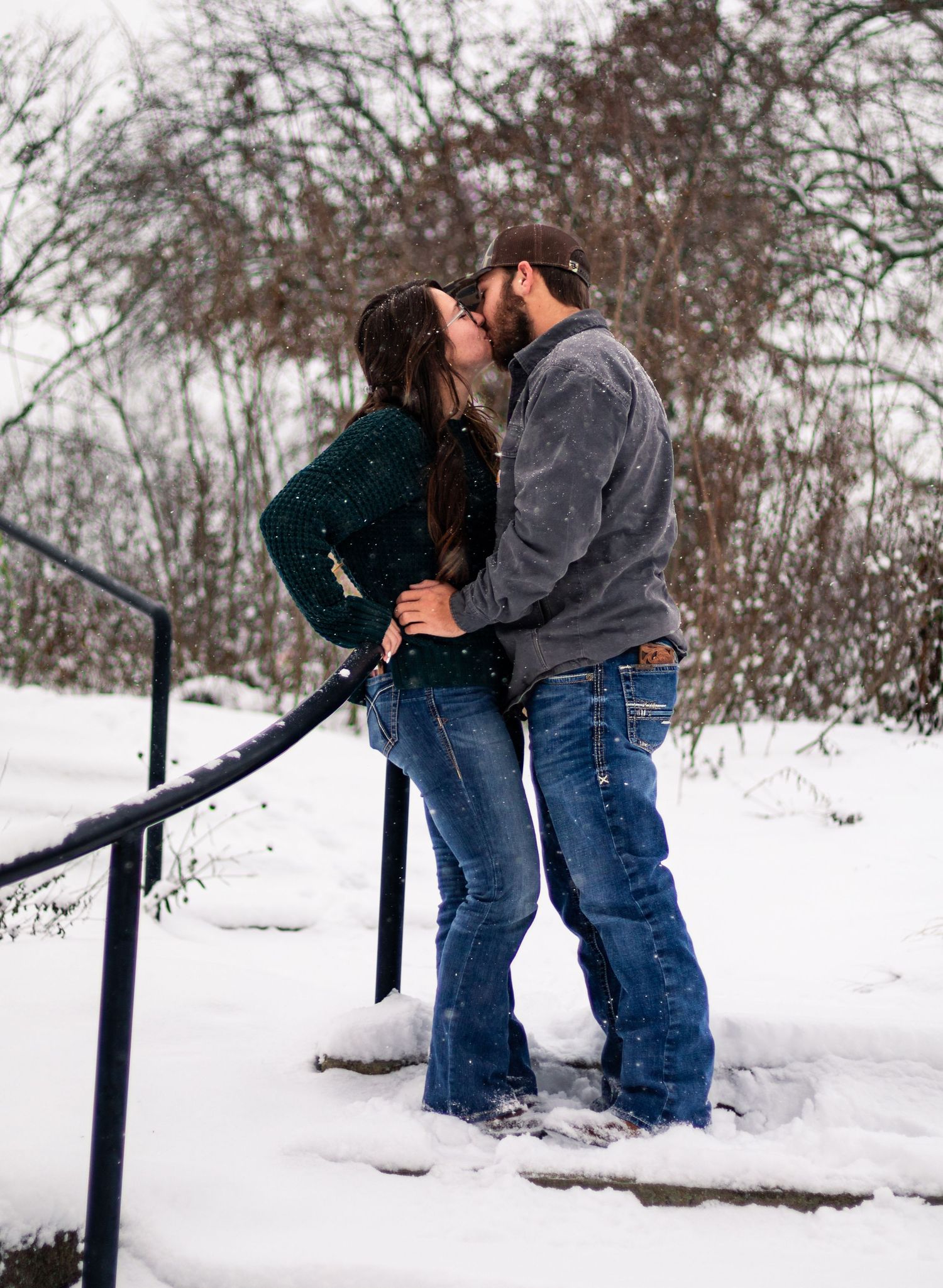 Romantic couple sharing a kiss on snowy steps during winter.