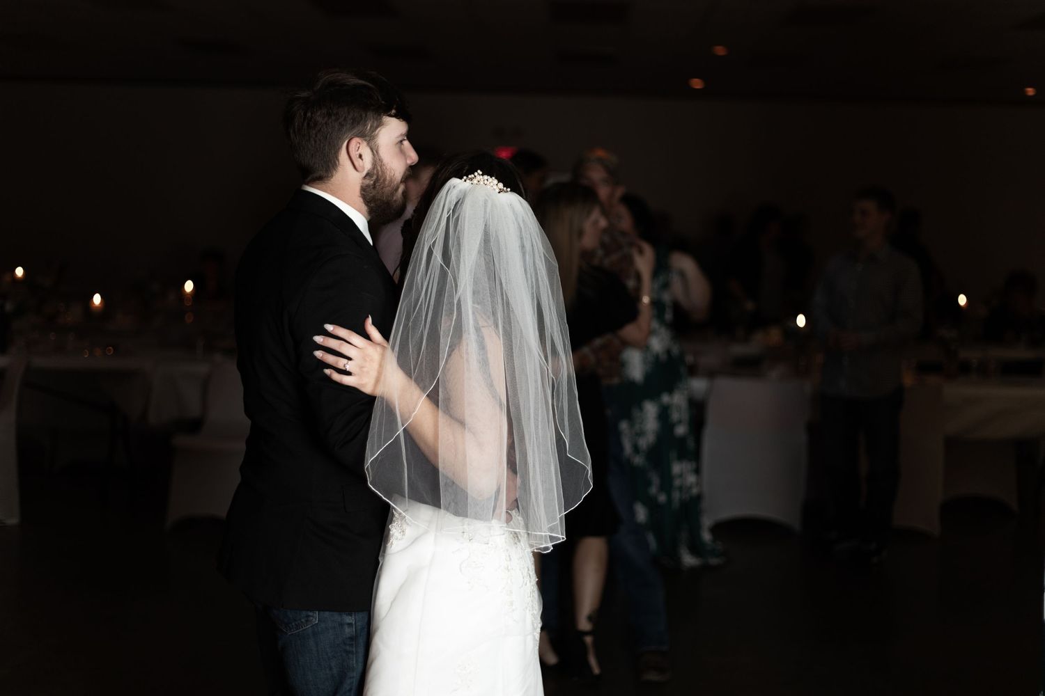 A couple shares their first dance at a wedding reception with guests watching in the background.