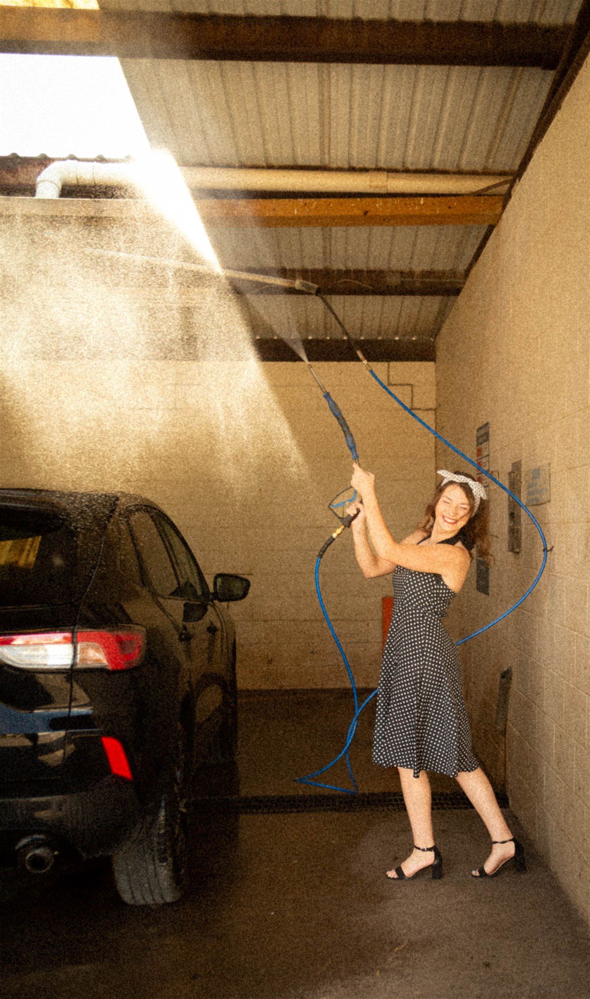 Person dances and poses in a sunlit garage space wearing a polka dot dress.