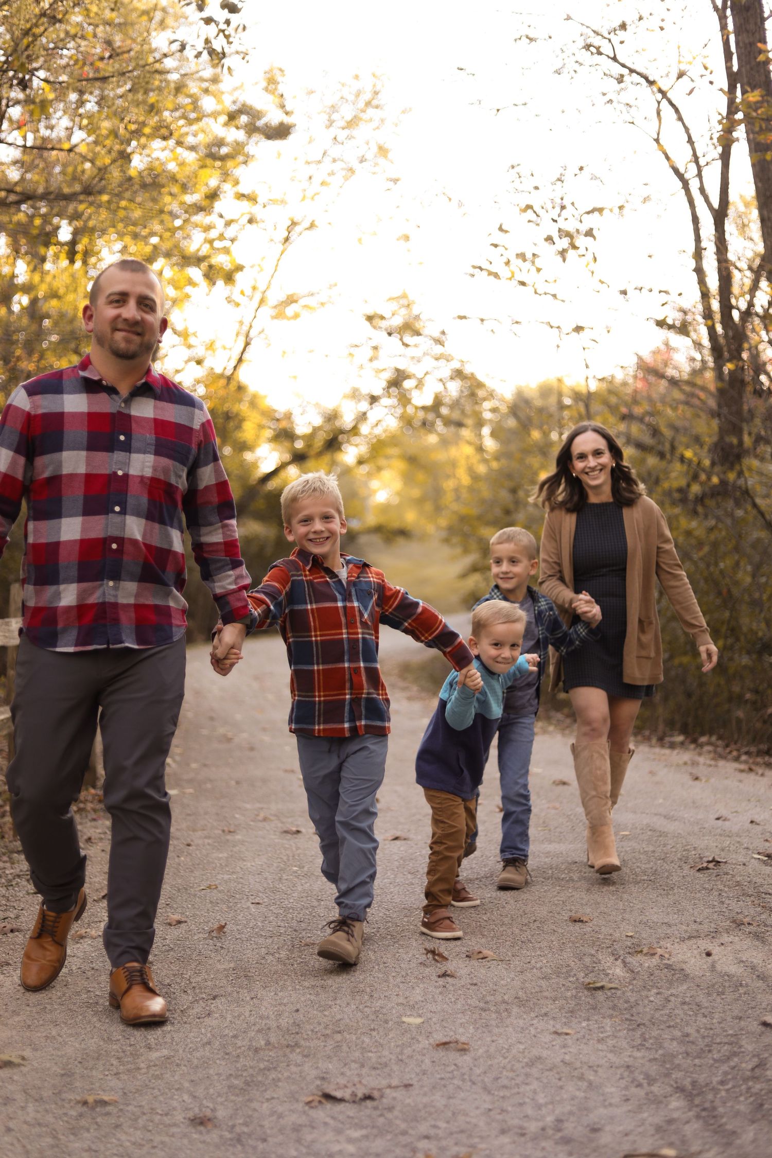 Family walking together on dirt path wearing matching plaid shirts during sunset.