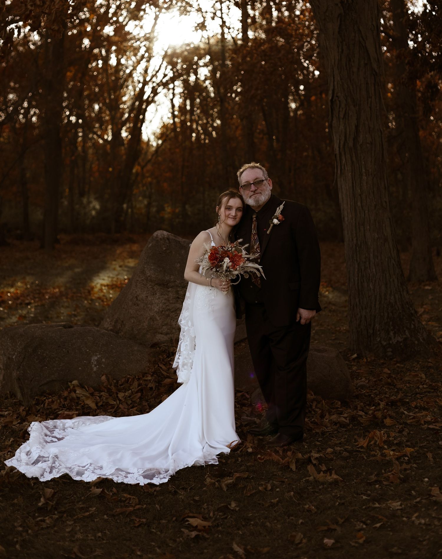 Wedding portraits in a wooded setting with dramatic autumn lighting and fallen leaves.