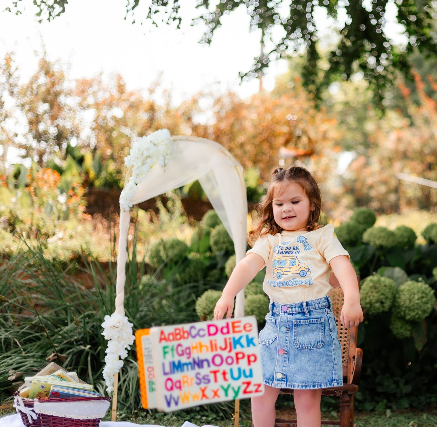 Child stands by lemonade stand with colorful sign in summer garden setting.
