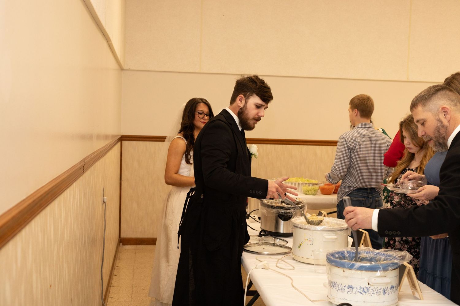 People gathered in a hallway or corridor serving and enjoying food at what appears to be a buffet-style event.