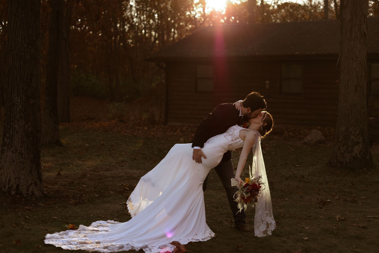 A romantic sunset wedding photo showing a couple in an elegant dip pose with a flowing white dress and bouquet.