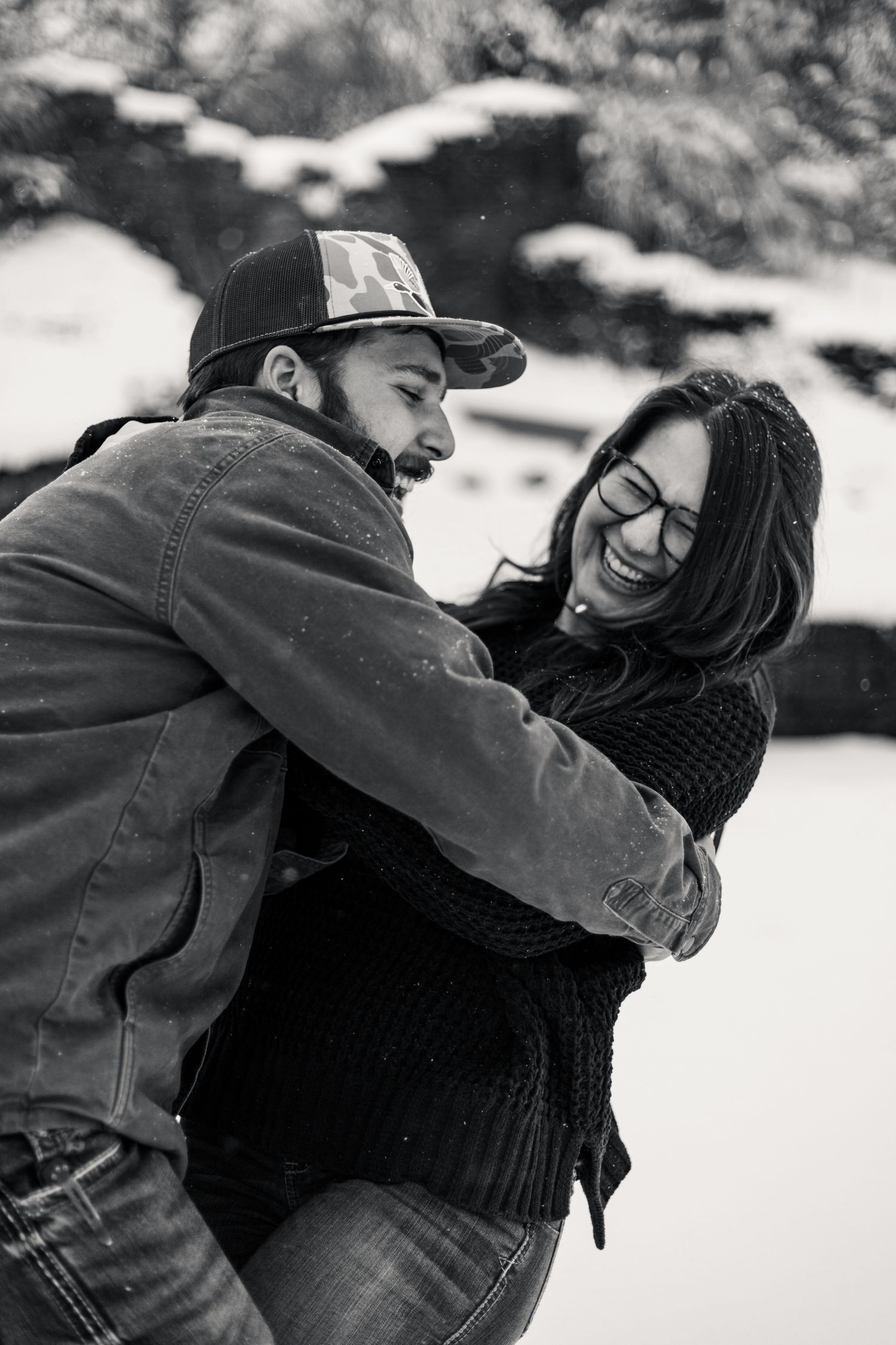 Black and white photo of couple embracing and laughing in a snowy setting.