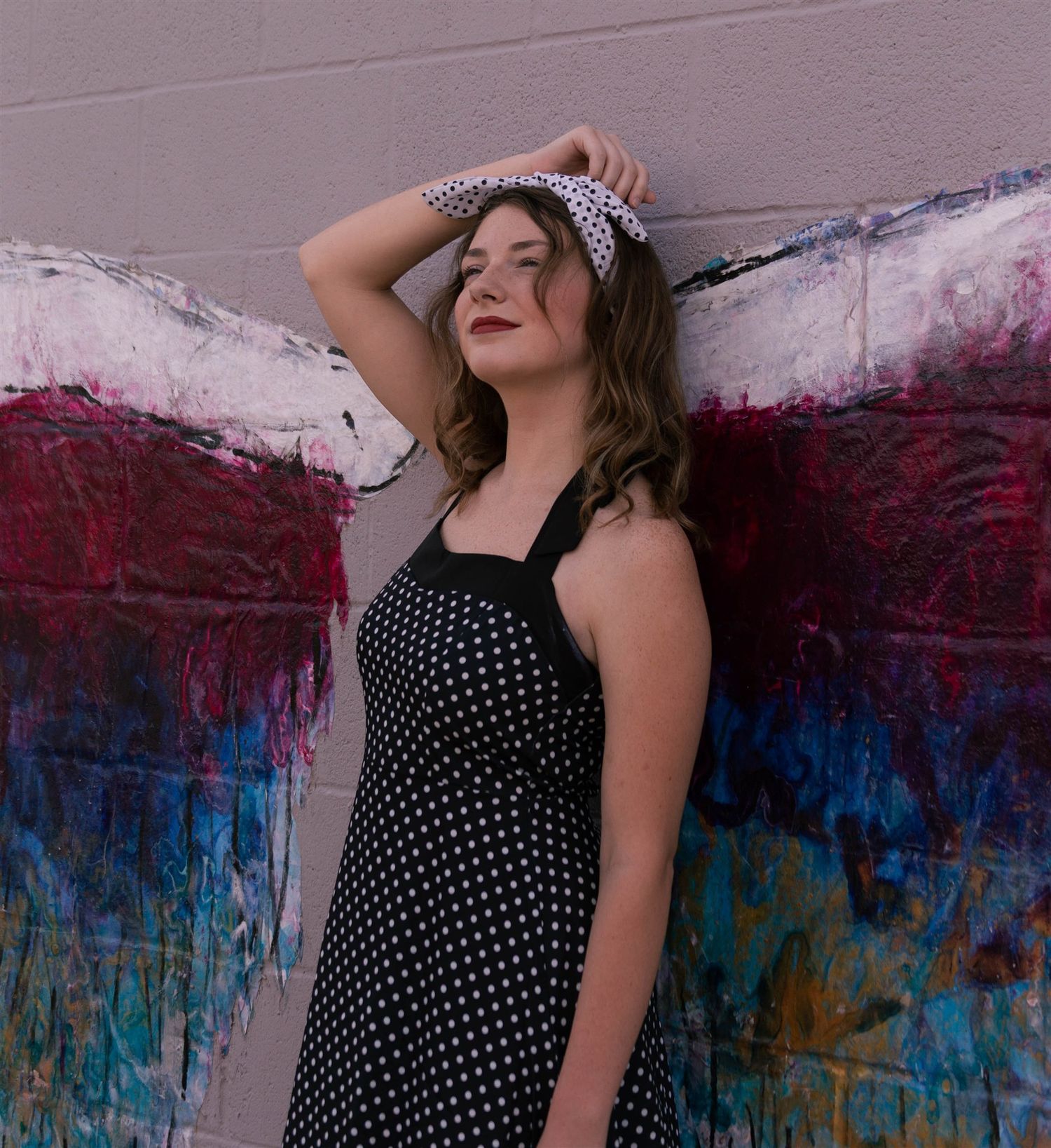 Person in a polka dot dress poses against a colorful painted wall background.