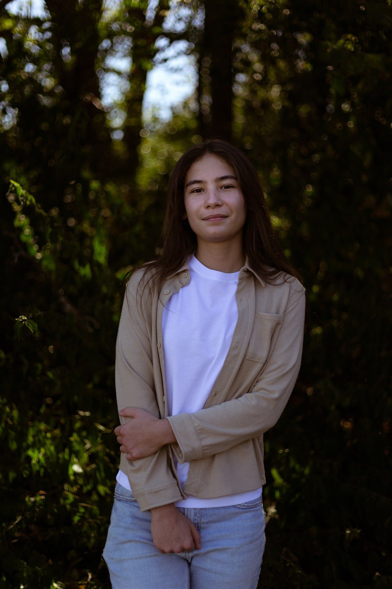 Person in casual attire poses outdoors in natural lighting wearing a beige jacket and white shirt.