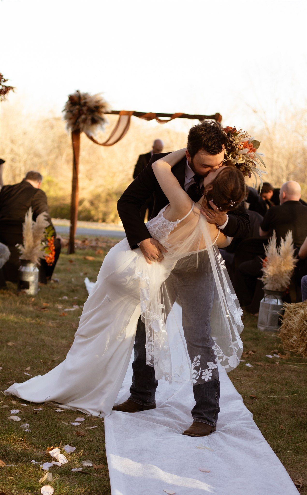Romantic couple dancing outdoors in wedding attire with flowing white dress at sunset.