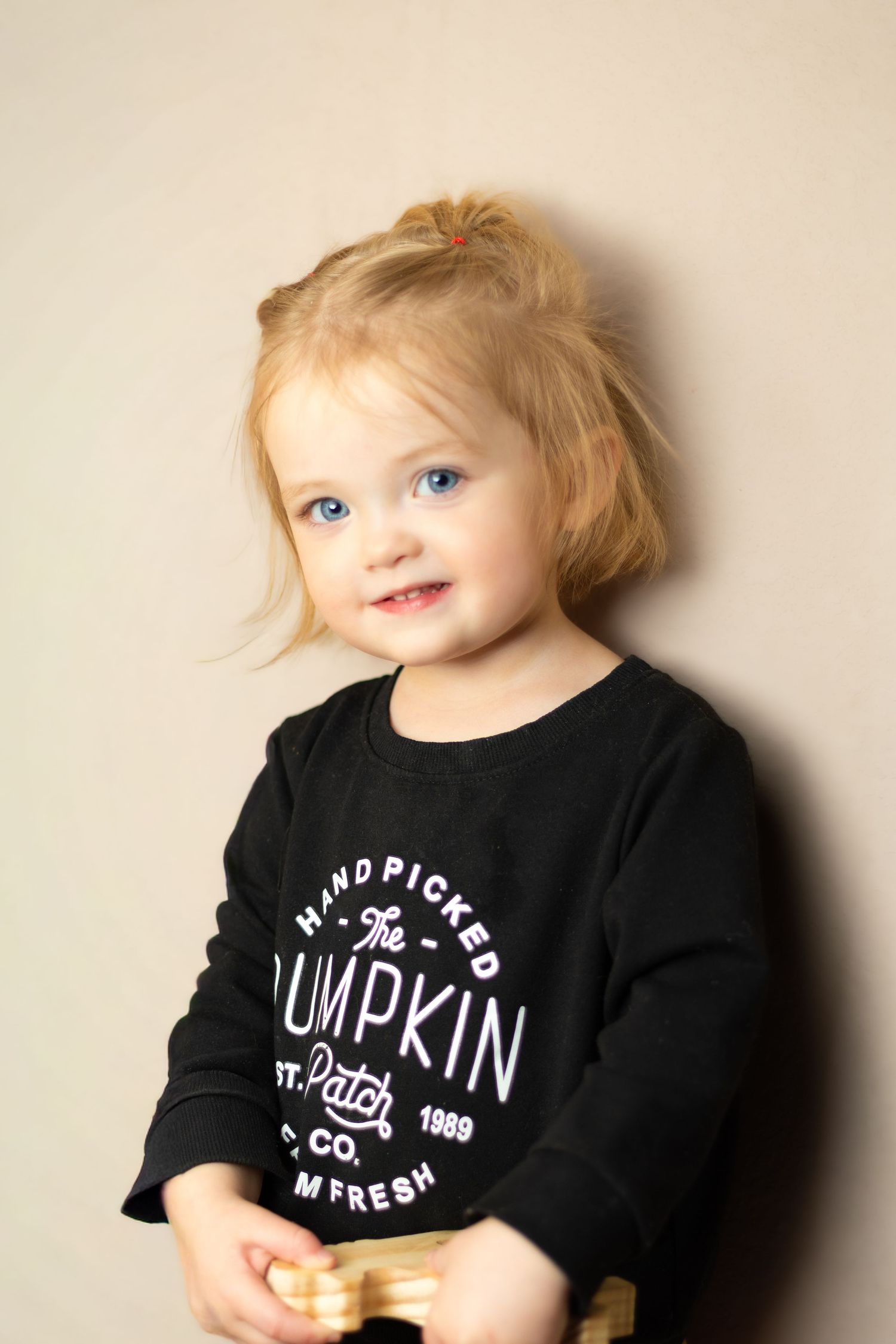 Young child wearing black t-shirt with pumpkin text design against neutral background.