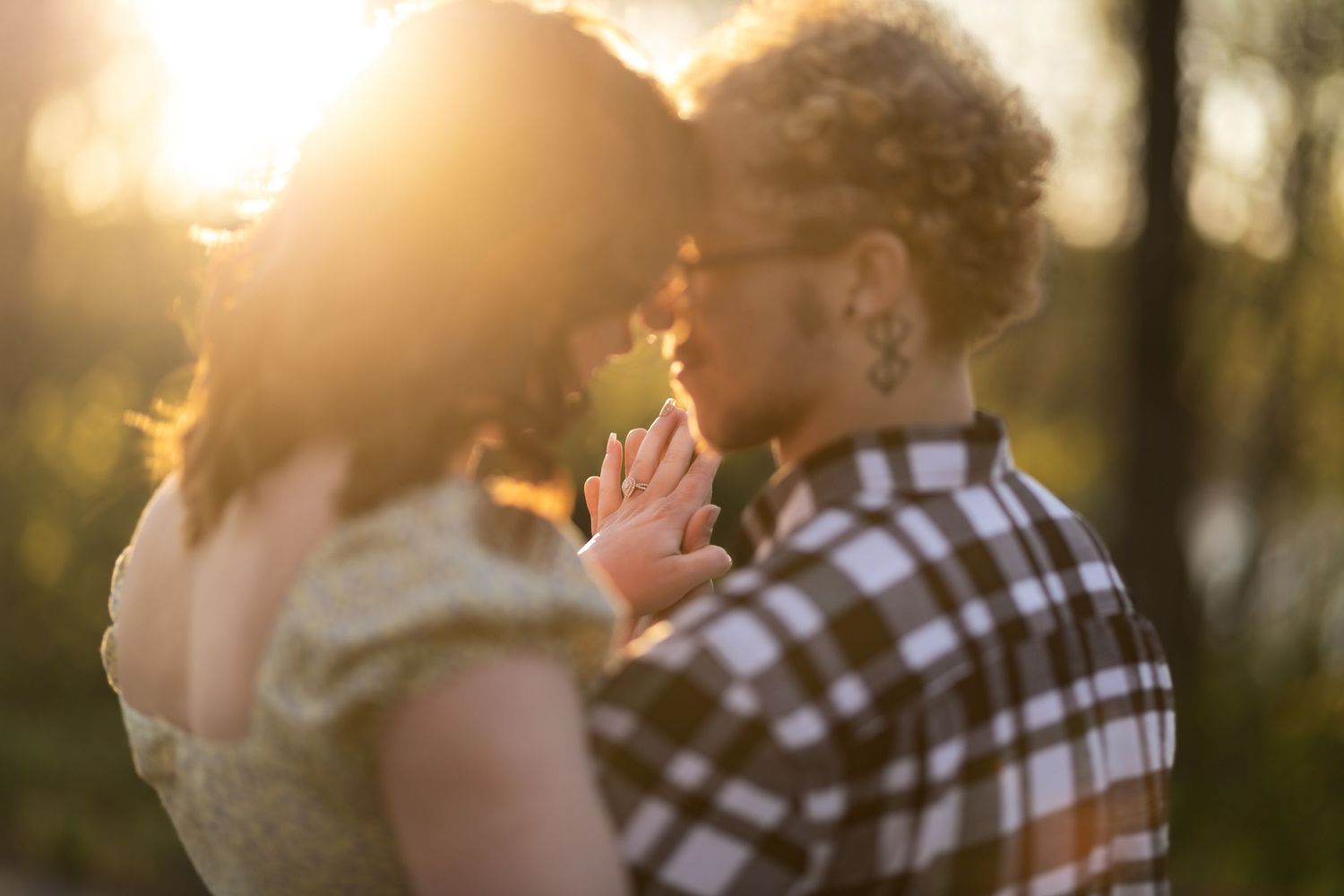 Couple sharing a romantic moment at golden hour sunset in a forest, woman in floral dress, man in plaid shirt.