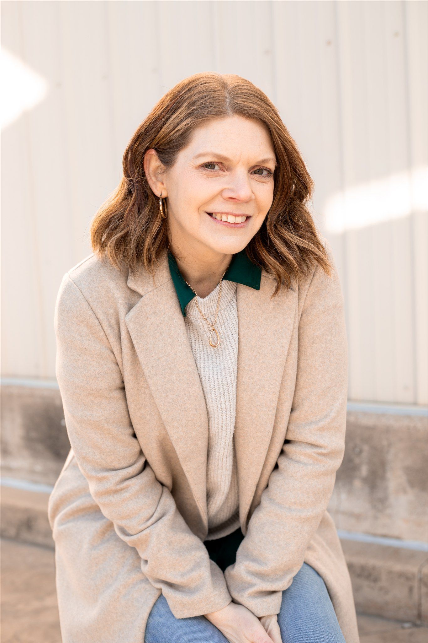 Professional portrait of person in beige coat and green collar sitting outdoors.