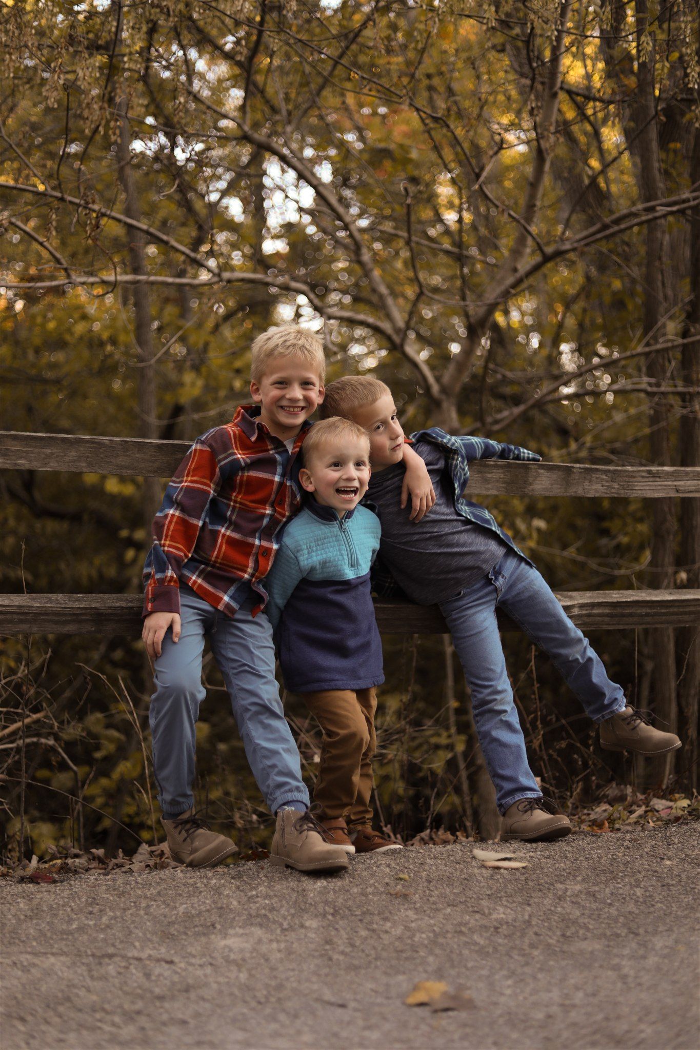 Children sitting on wooden fence during golden hour with autumn foliage in background.