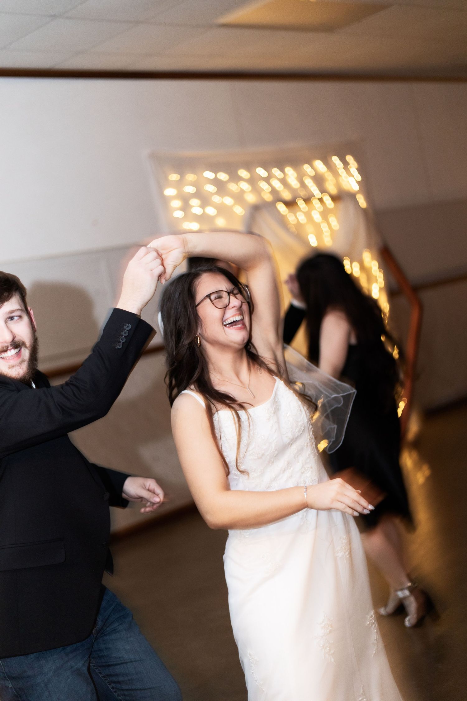 bride and groom dancing and having fun at a party with string lights glowing in the background.