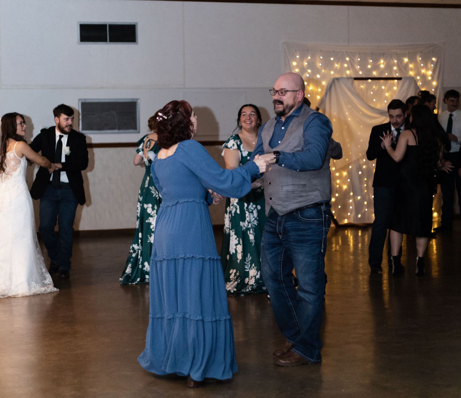 Guests dancing and celebrating at a wedding reception with twinkle lights and decorations in the background.