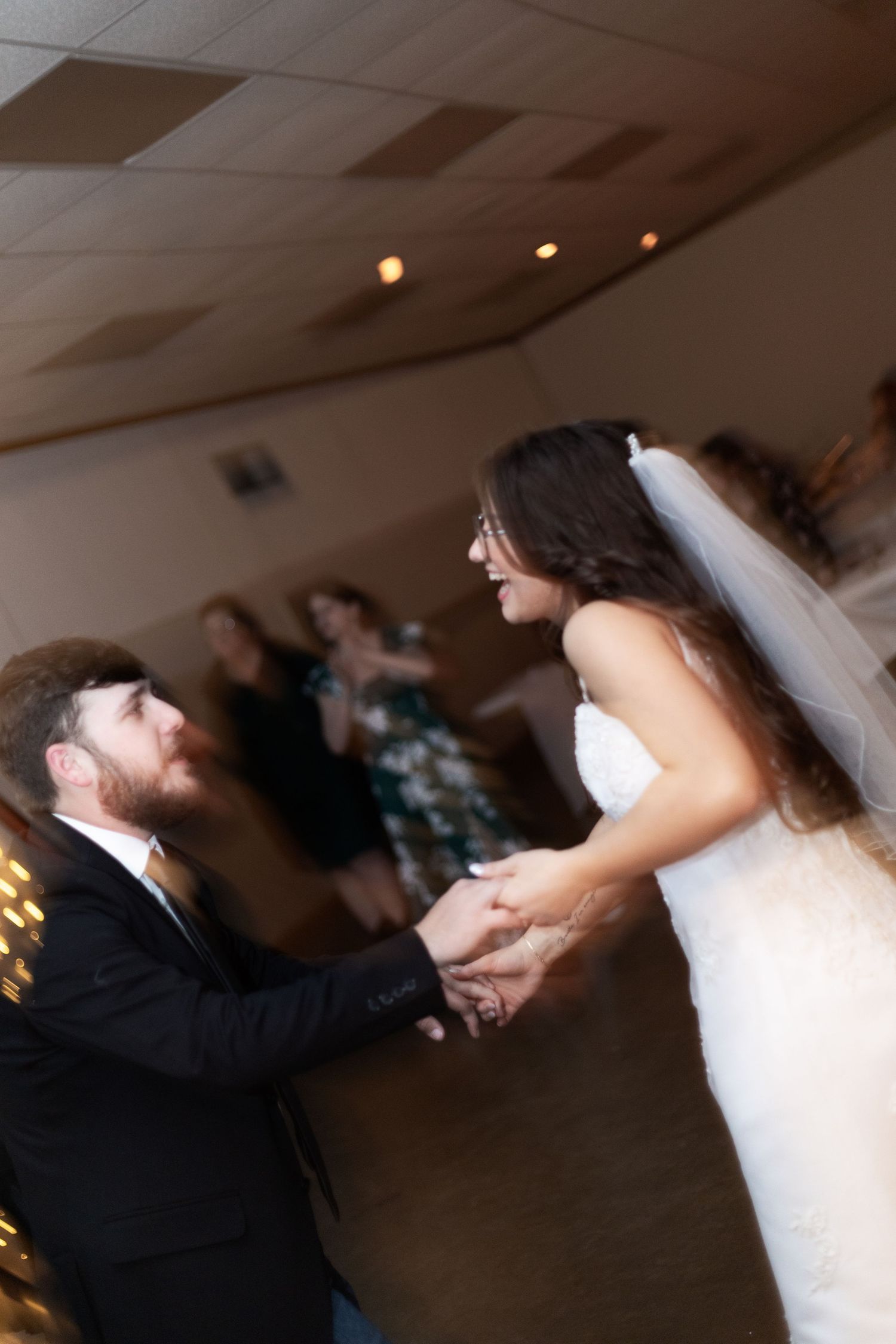 Bride and groom share their first dance at wedding reception, holding hands and smiling joyfully.