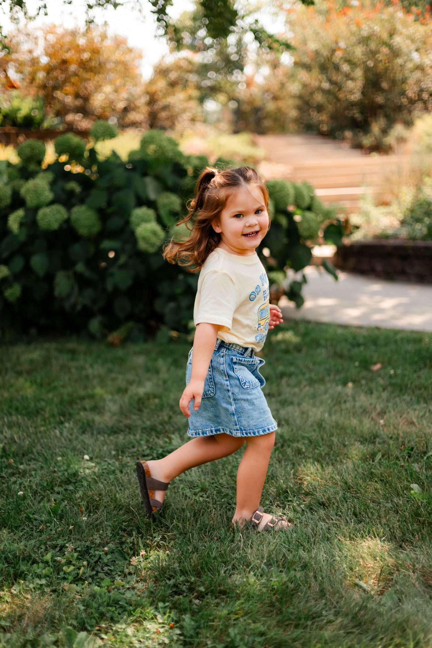 Young child in denim skirt plays joyfully in garden during autumn.