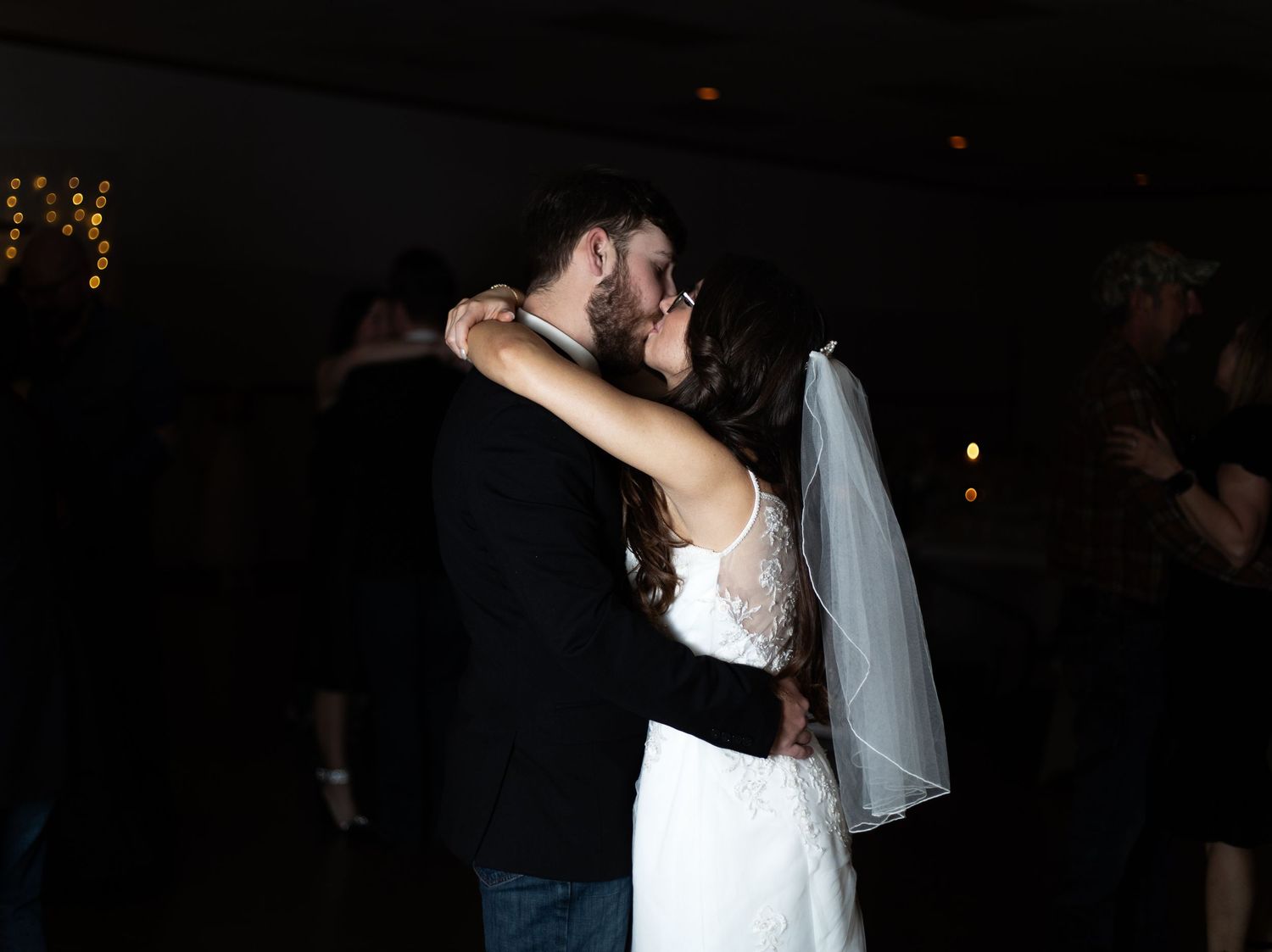 A couple shares their first dance at a dimly lit wedding reception, with the bride in white and groom in black.