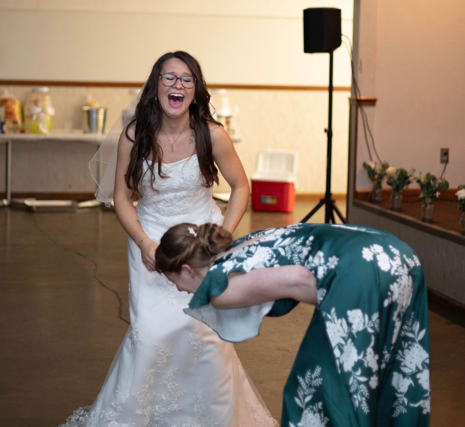 Two people dancing and laughing together, one wearing a white dress and another in teal floral print.