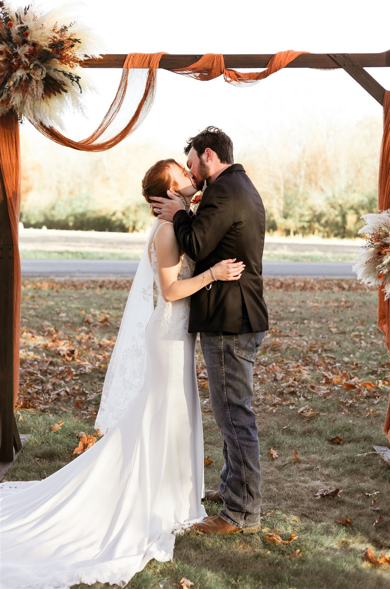 Wedding couple embracing under wooden arch decorated with autumn flowers and foliage.