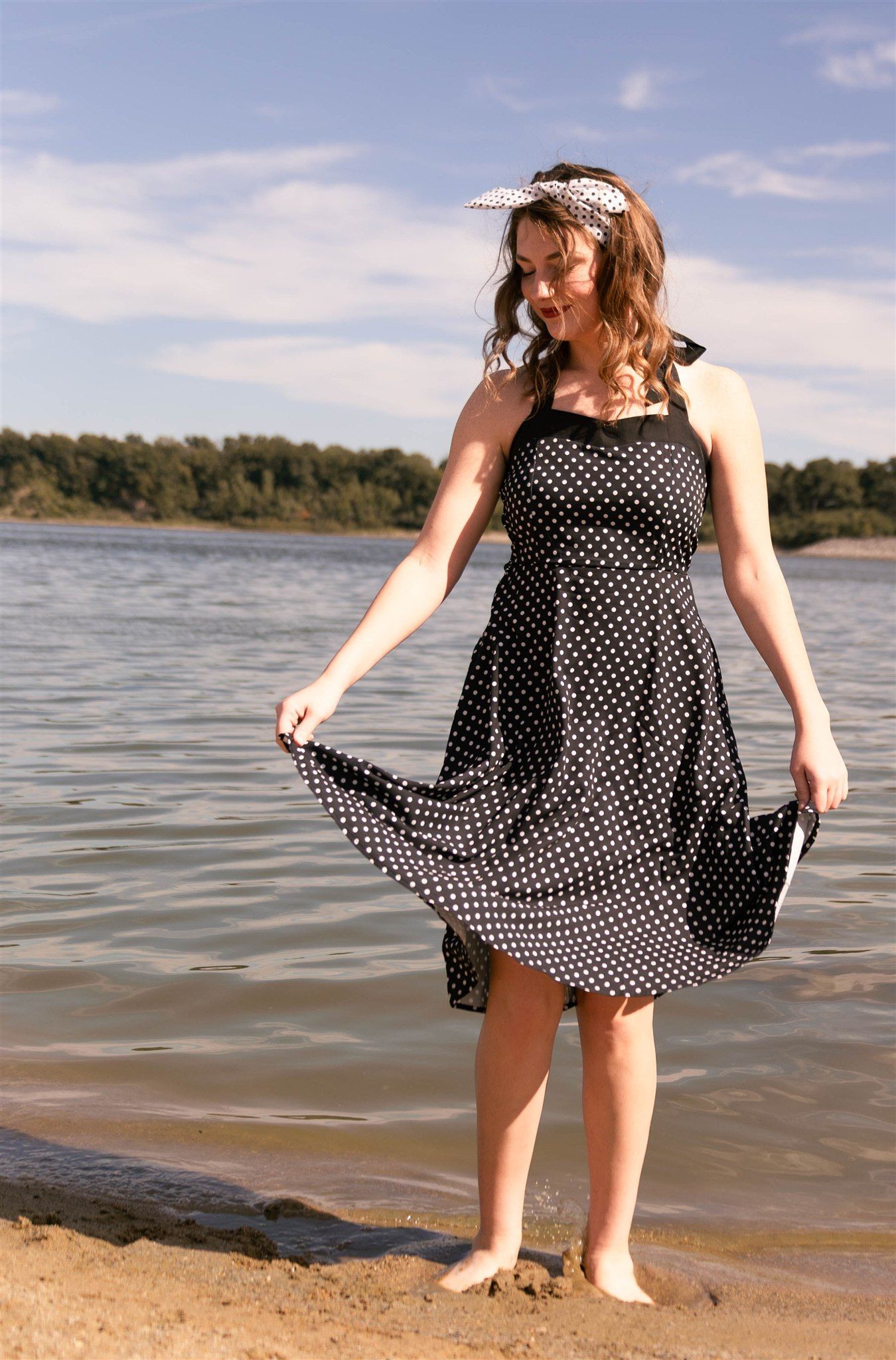 Person in a polka dot dress plays at the edge of a lake on a sunny day.