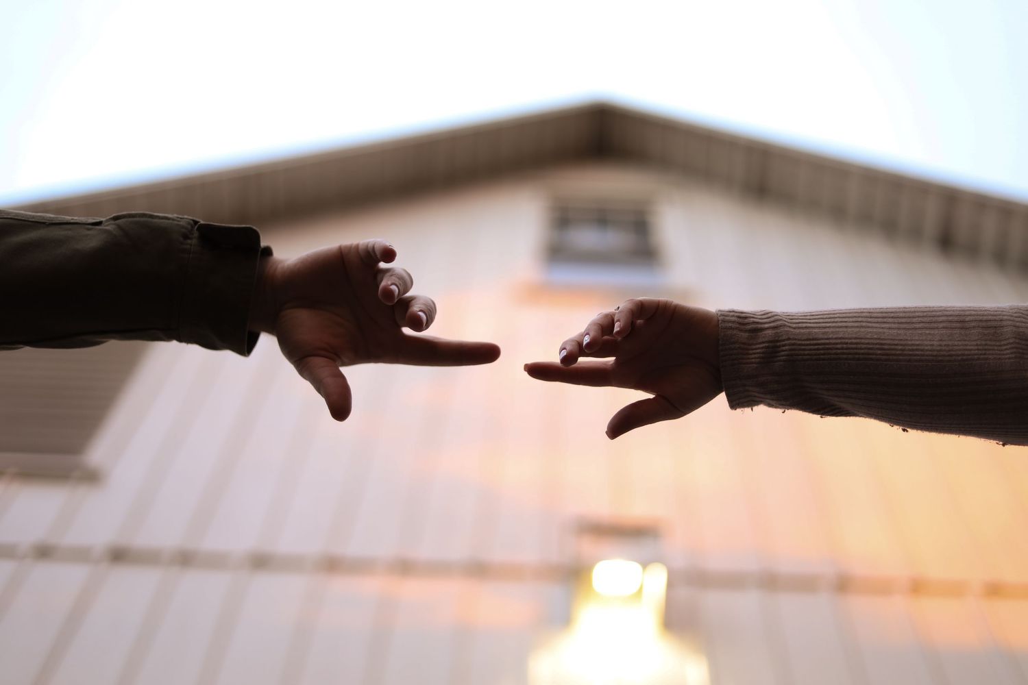 Silhouetted hands reach toward each other against a bright background.