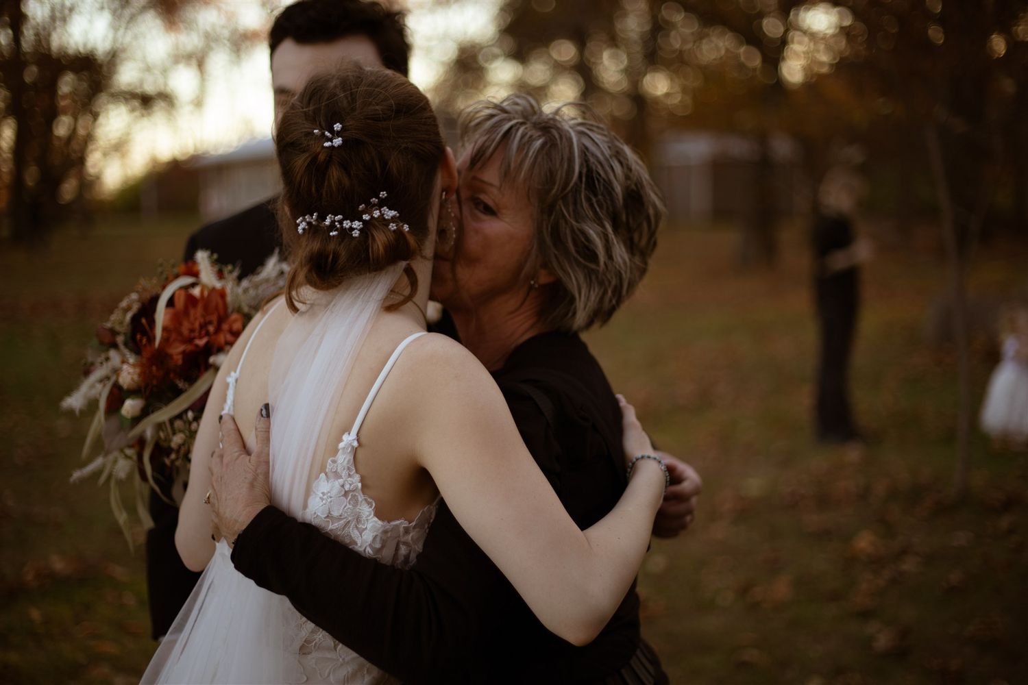 Intimate wedding moment captured in a forest with golden sunlight filtering through trees.