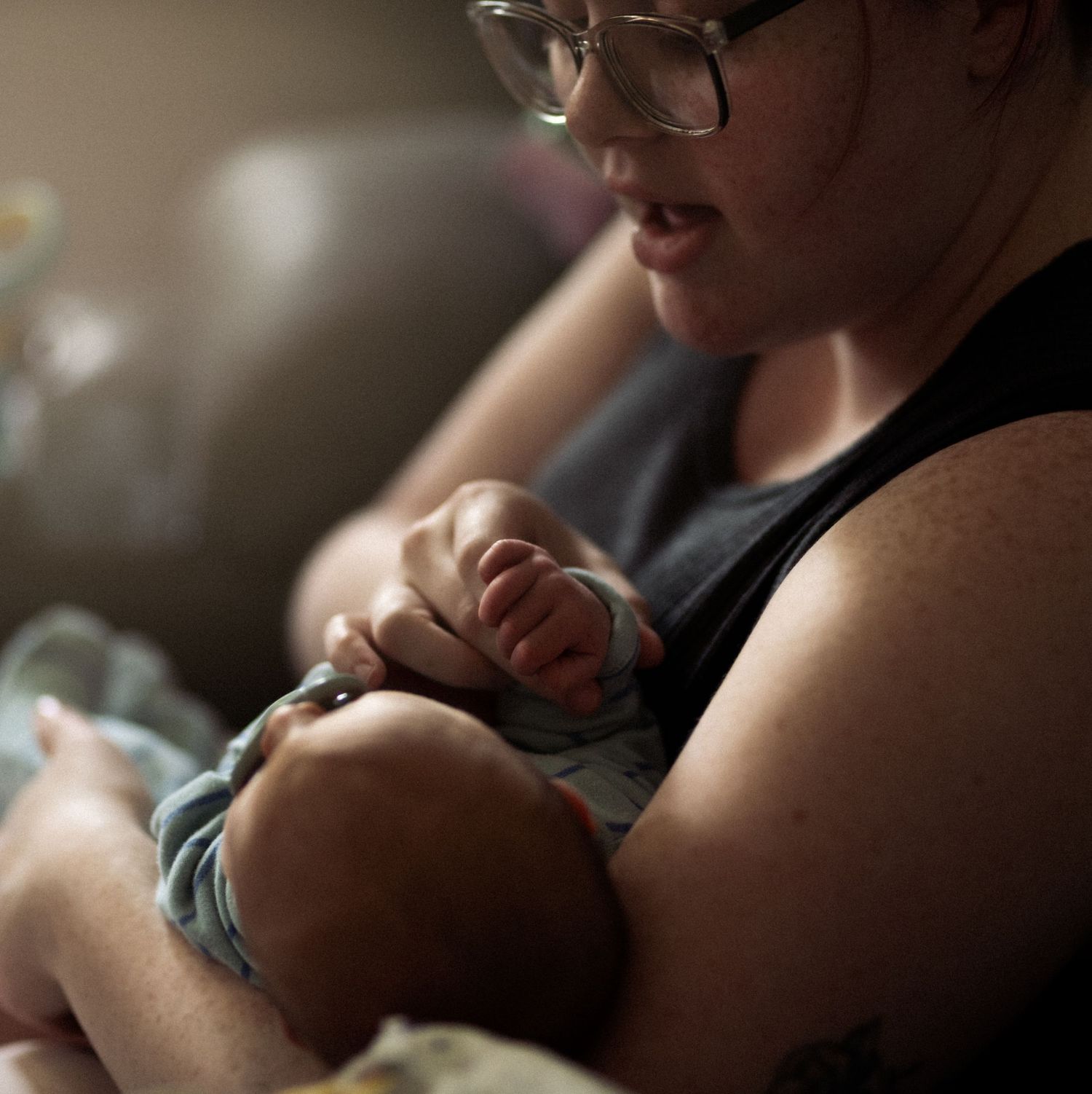 Mother with glasses tenderly holding her newborn baby while sitting in a chair after birth.