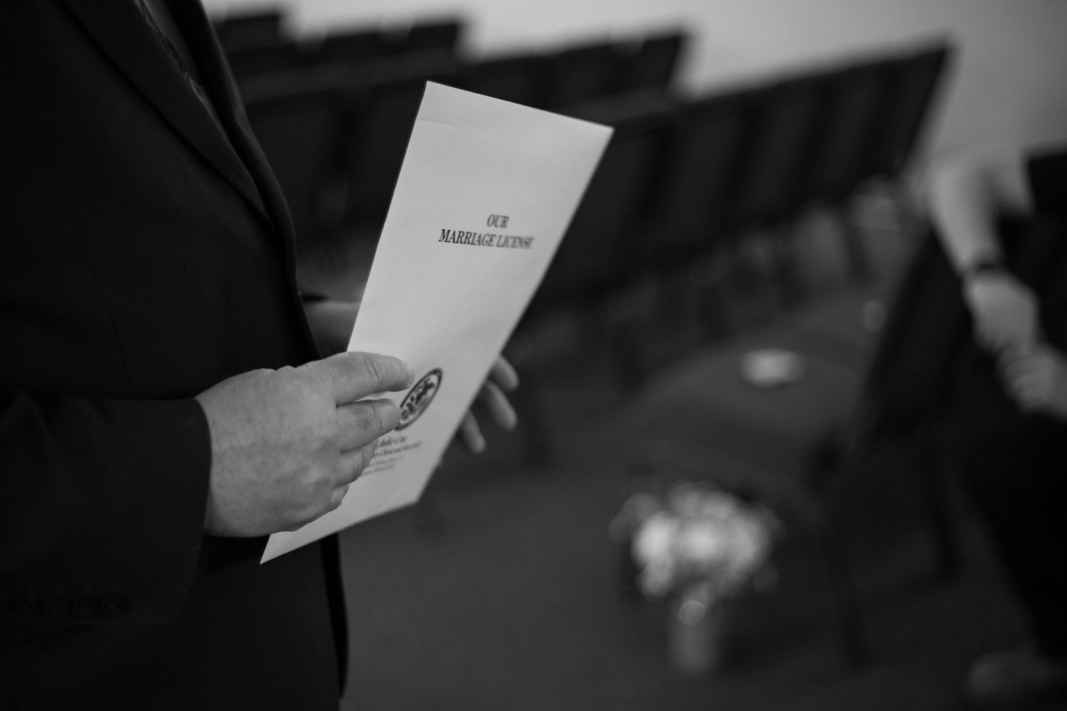 Person in suit holding a marriage ceremony program booklet in a black and white wedding venue photo.