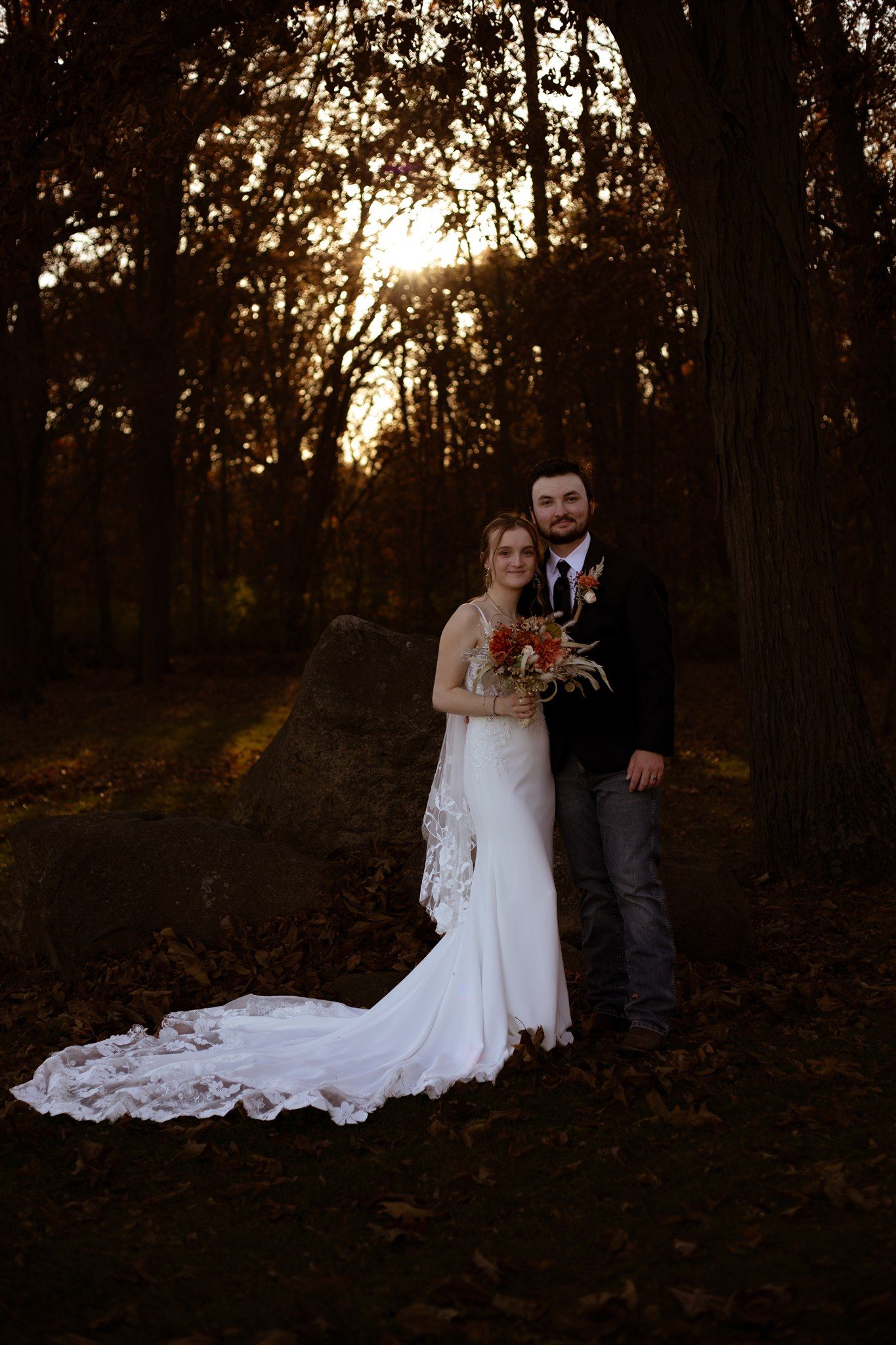 Elegant wedding couple poses among trees during golden hour in autumn forest.
