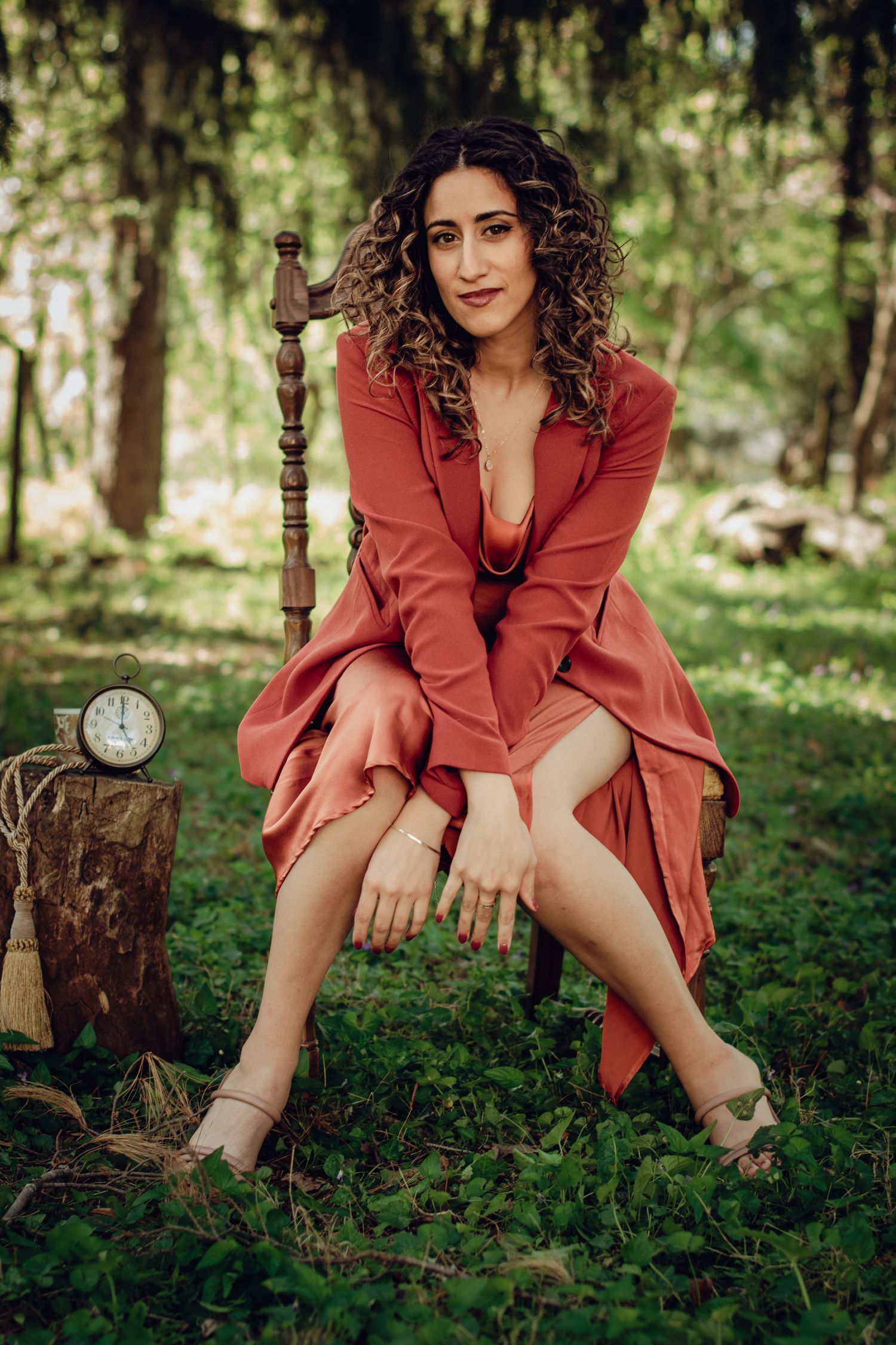 Artistic portrait in coral dress sitting among forest greenery.