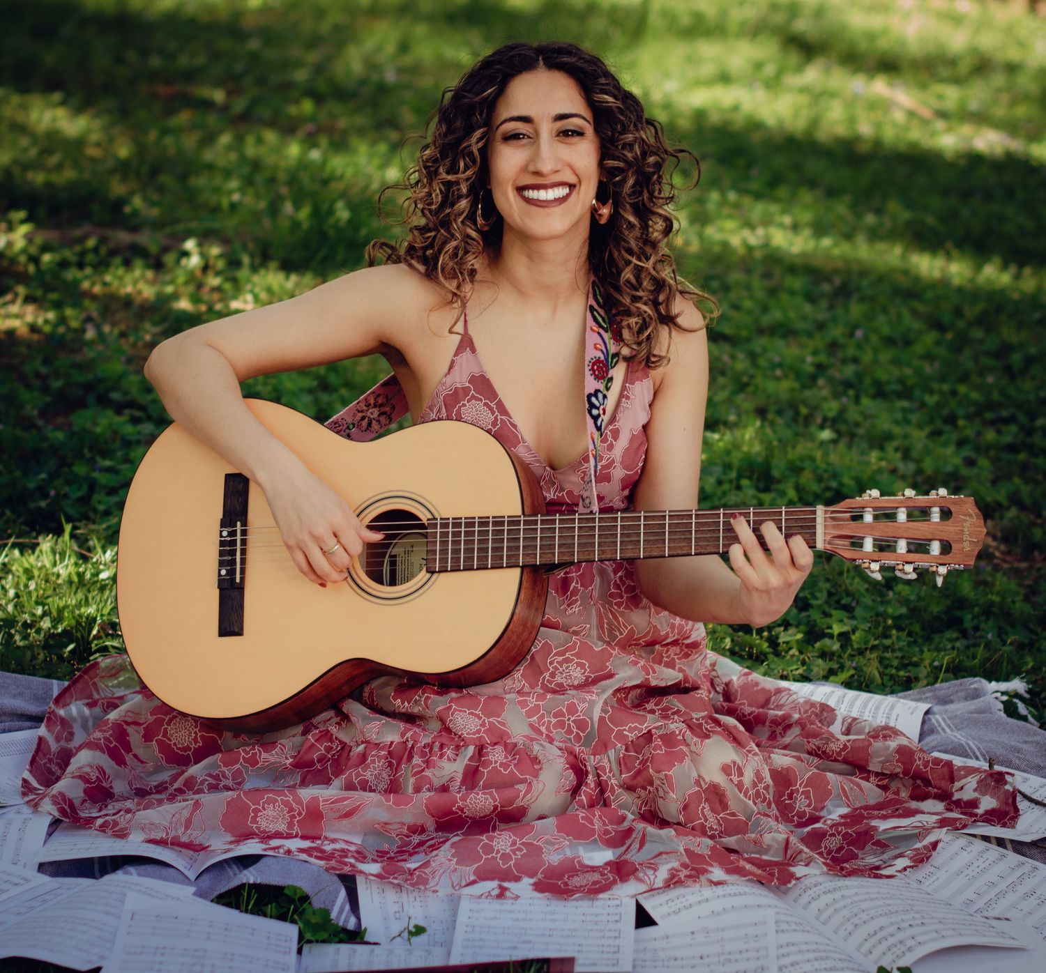 Woman smiling with acoustic guitar with sheet music scattered on sunny grass lawn. Professional portrait photography.