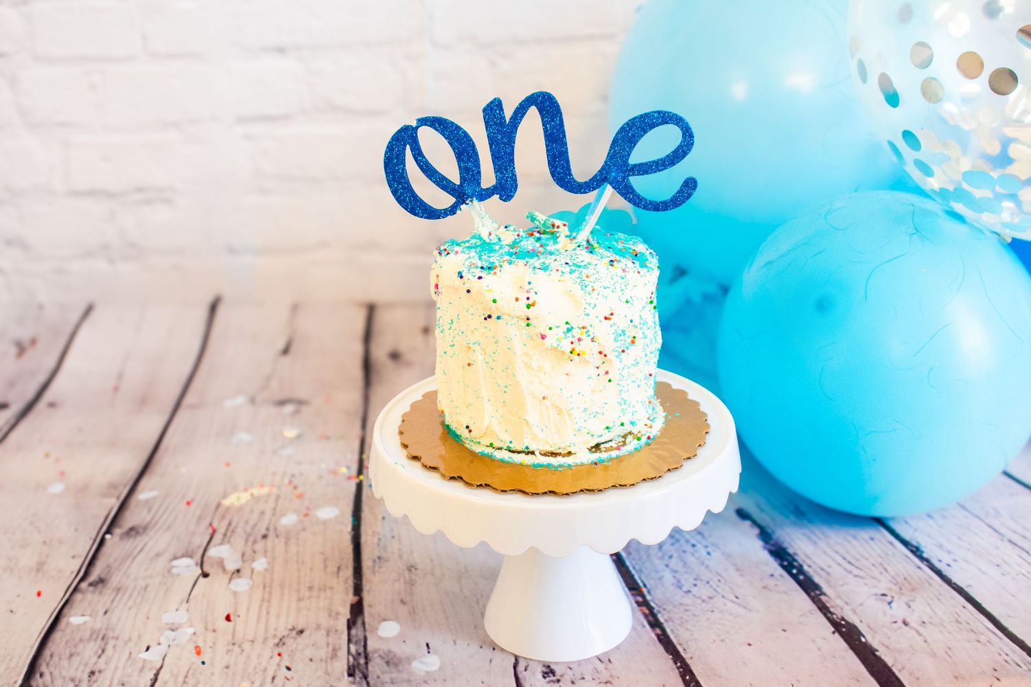 White cake covered with sprinkles with a blue one written in cursive added to the top. Professional photography.