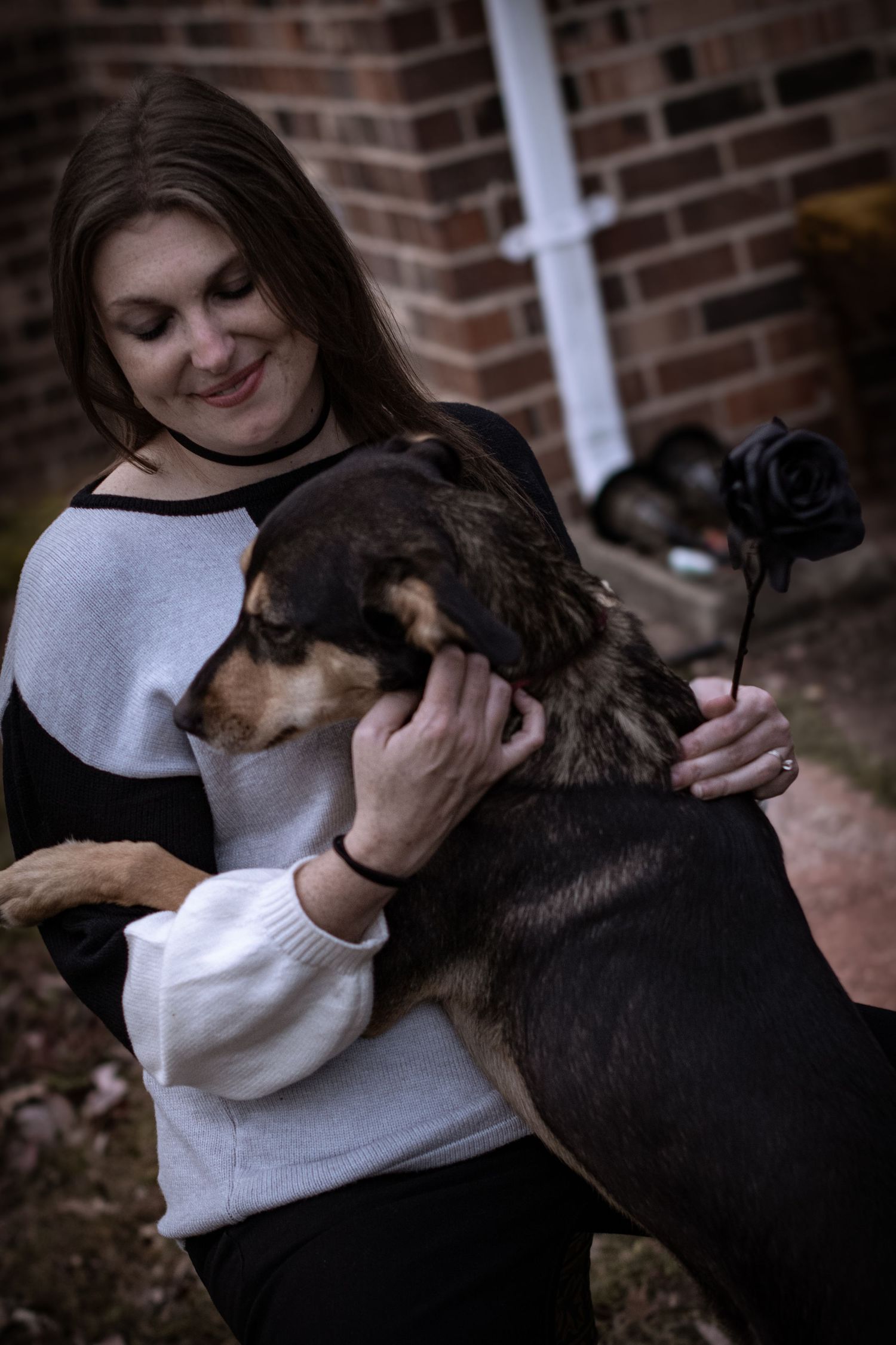 Smiling woman in casual outfit lovingly embraces large black and tan dog outdoors.
