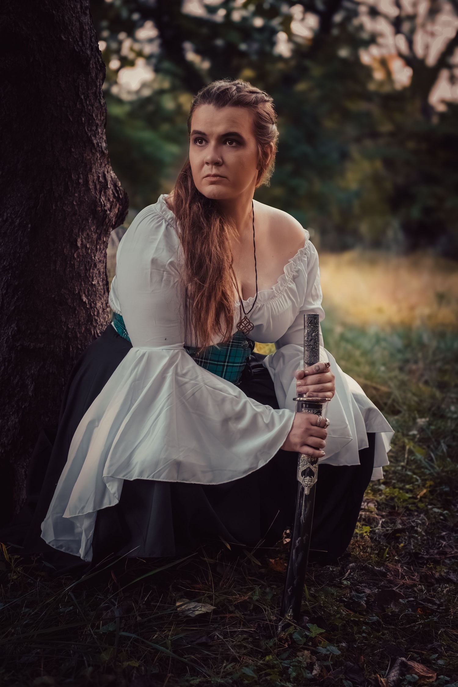 A person in a medieval-style white dress crouches near a tree trunk while holding a glass of wine in a forest setting.