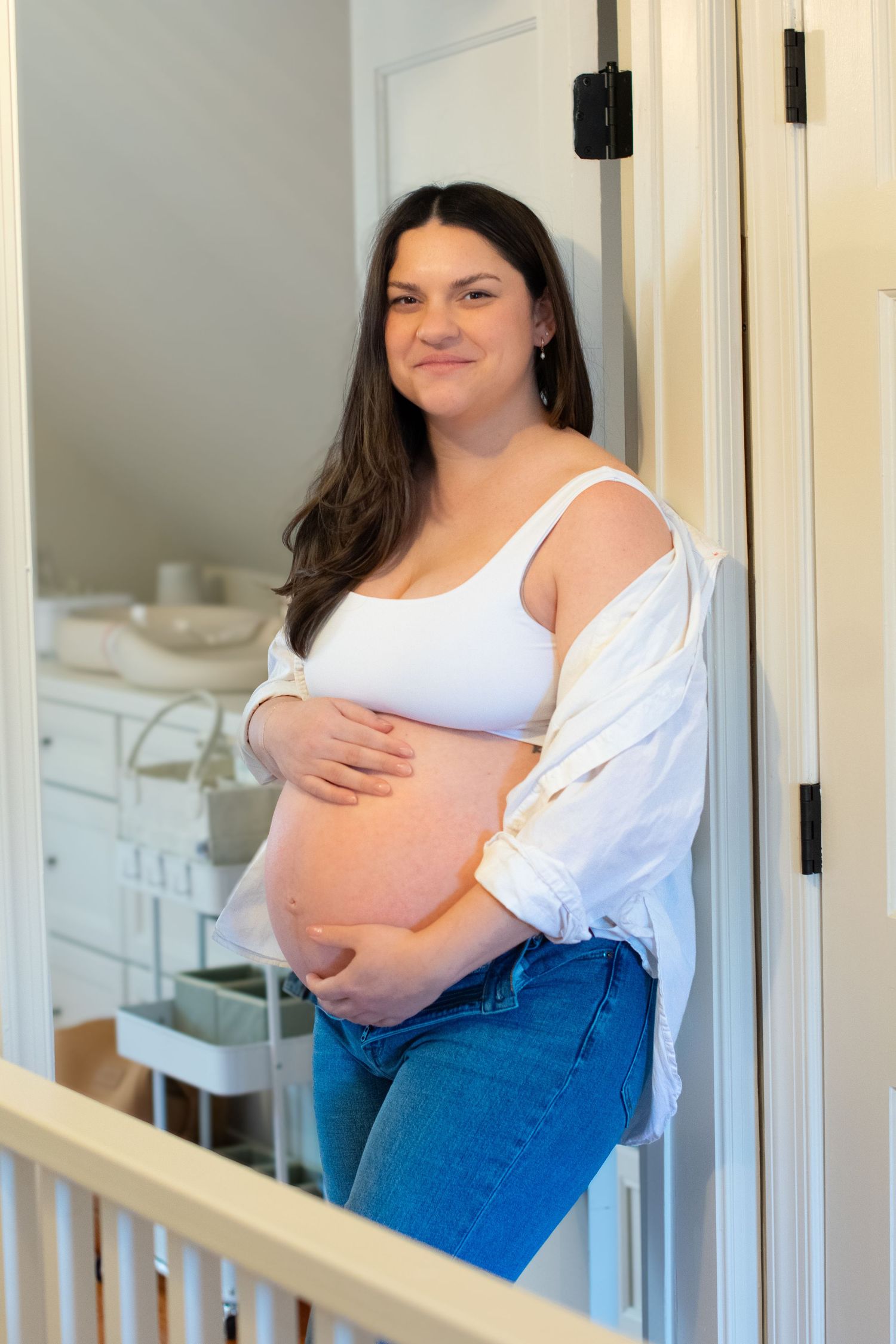 Woman in casual attire leaning against doorframe, posing for maternity photo in a modern home interior with white walls.
