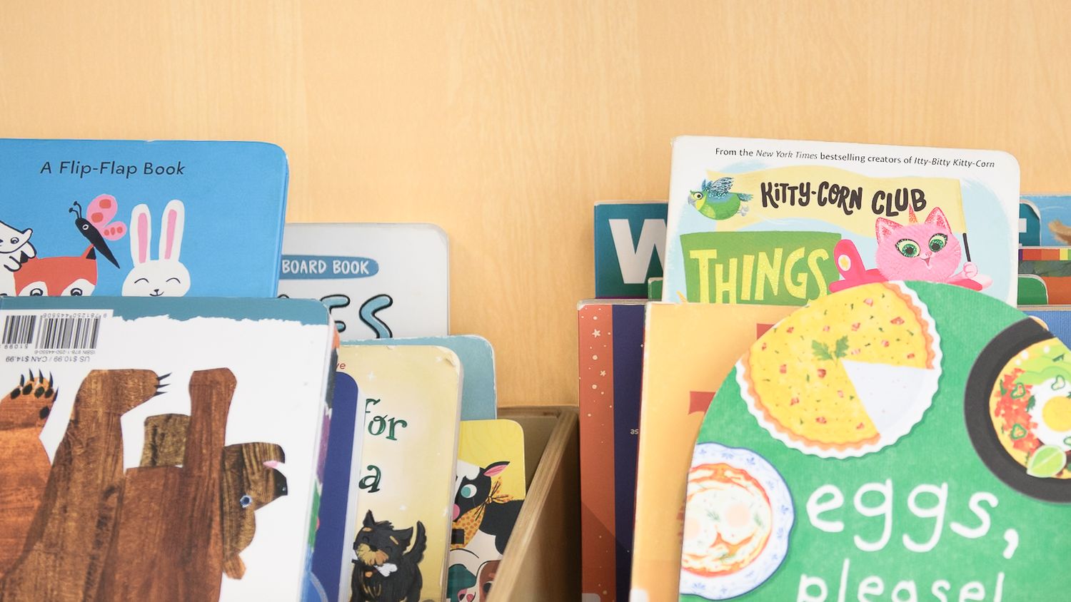 Colorful collection of children's picture books displayed upright on a wooden shelf.