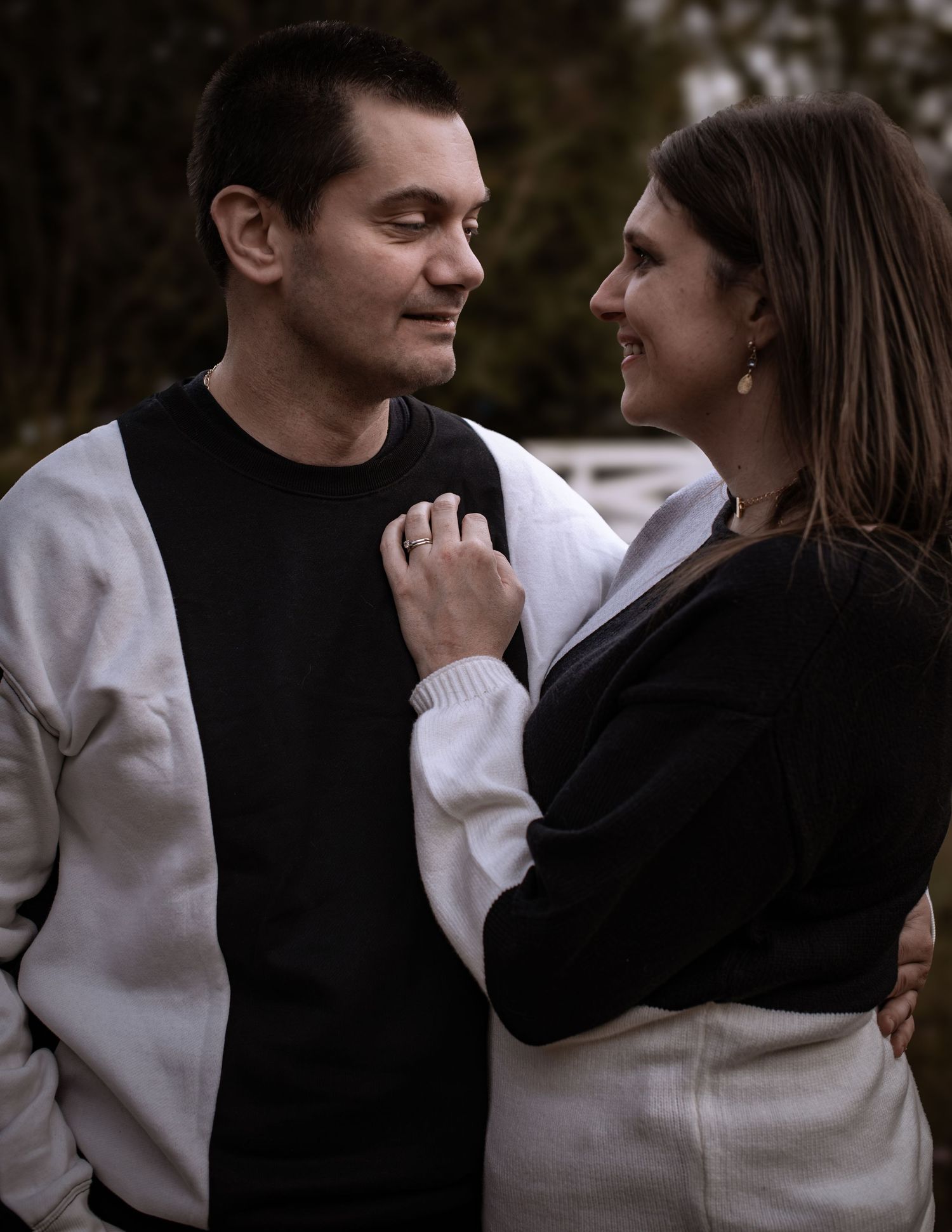 Couple in casual black and white outfits share a tender moment outdoors.