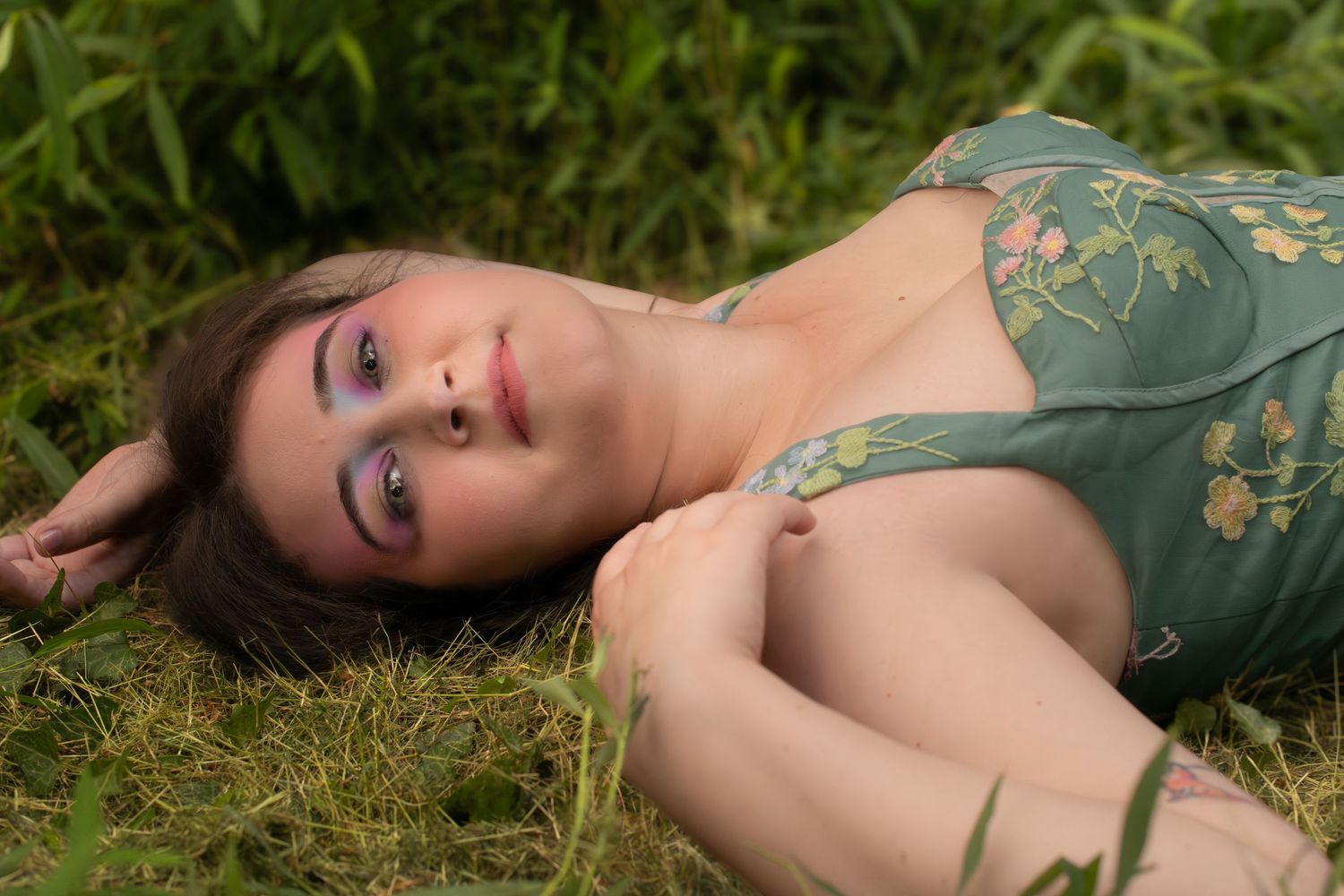 Figure in green floral dress lying in grass during outdoor photo session.