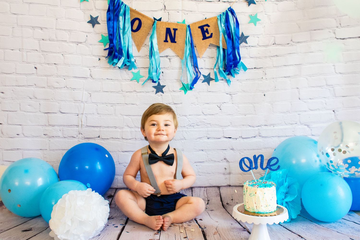 Small boy wearing a bow tie and suspenders smiling under a blue banner that reads 