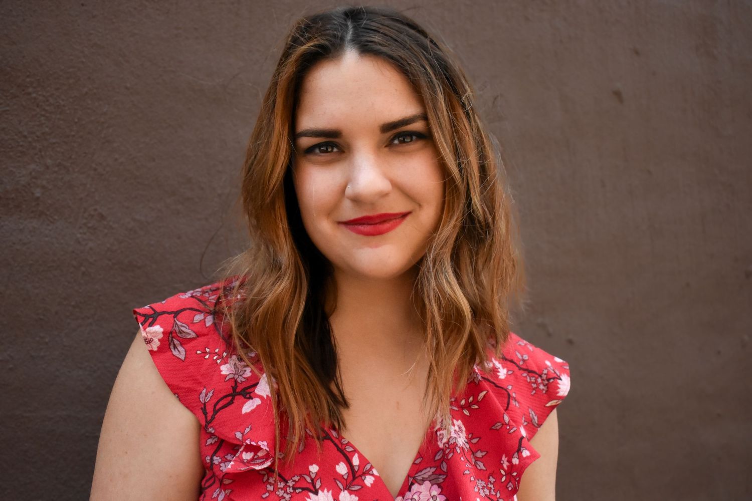 Portrait against brown wall wearing red floral dress with ruffled sleeves.