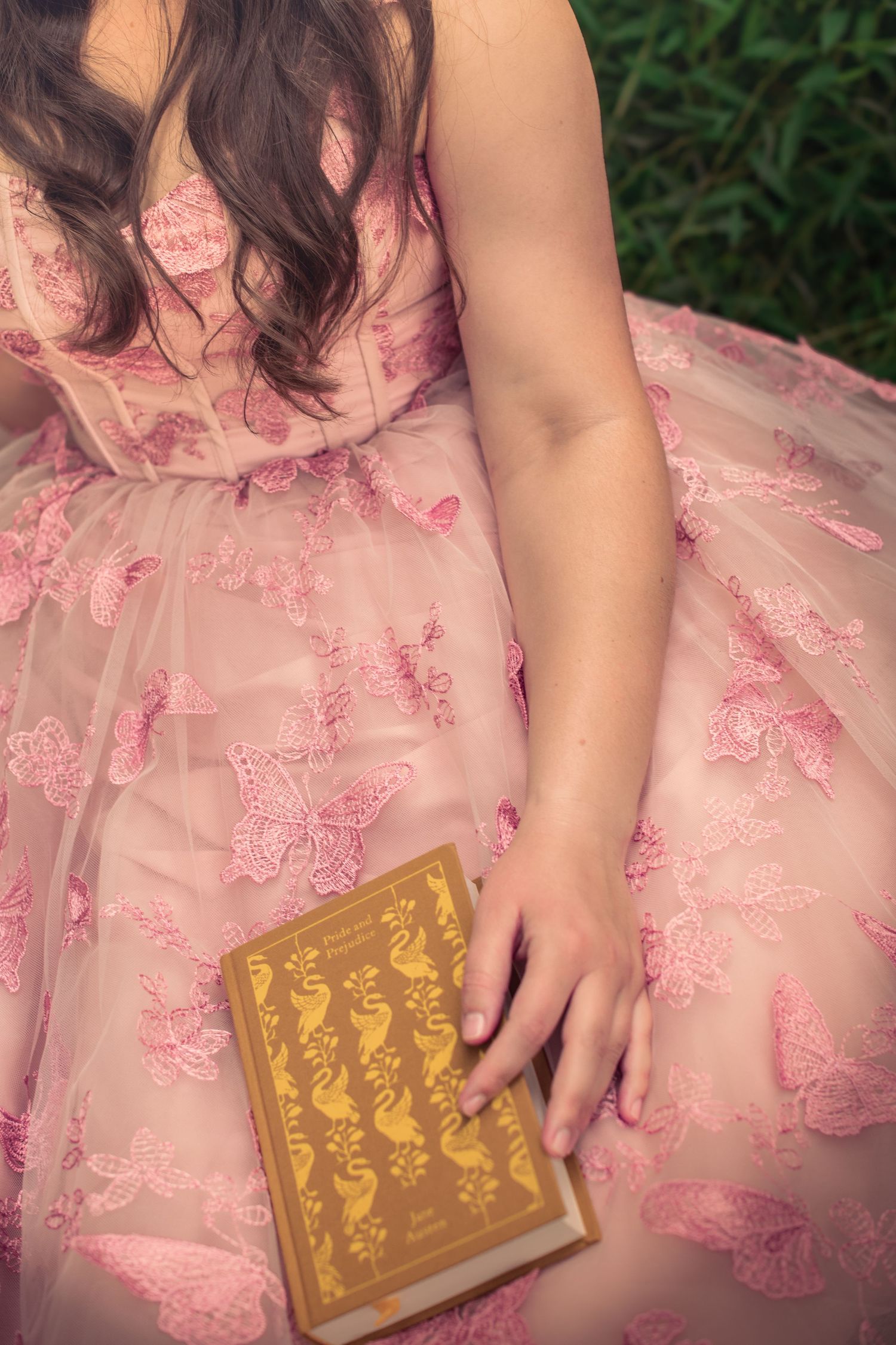 A pink lace dress with tulle skirt is shown alongside a vintage gold-embossed book in a garden setting.