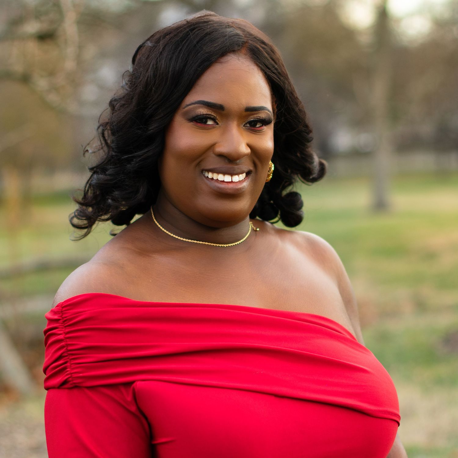 Headshot of a woman in vibrant red dress against natural outdoor setting.
