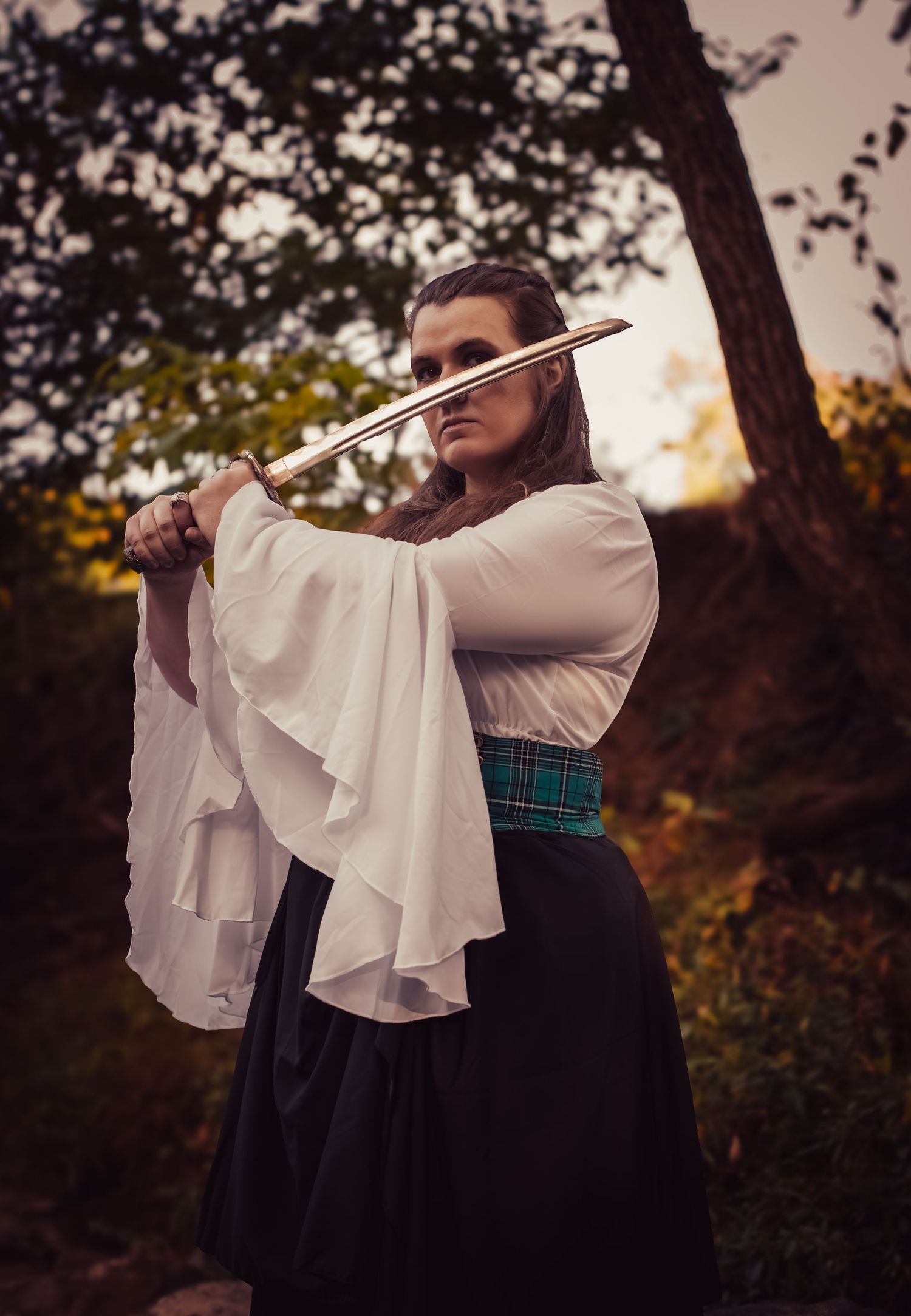 A dramatic series of photos showing someone holding a sword against a moody outdoor backdrop with ruffle sleeves.