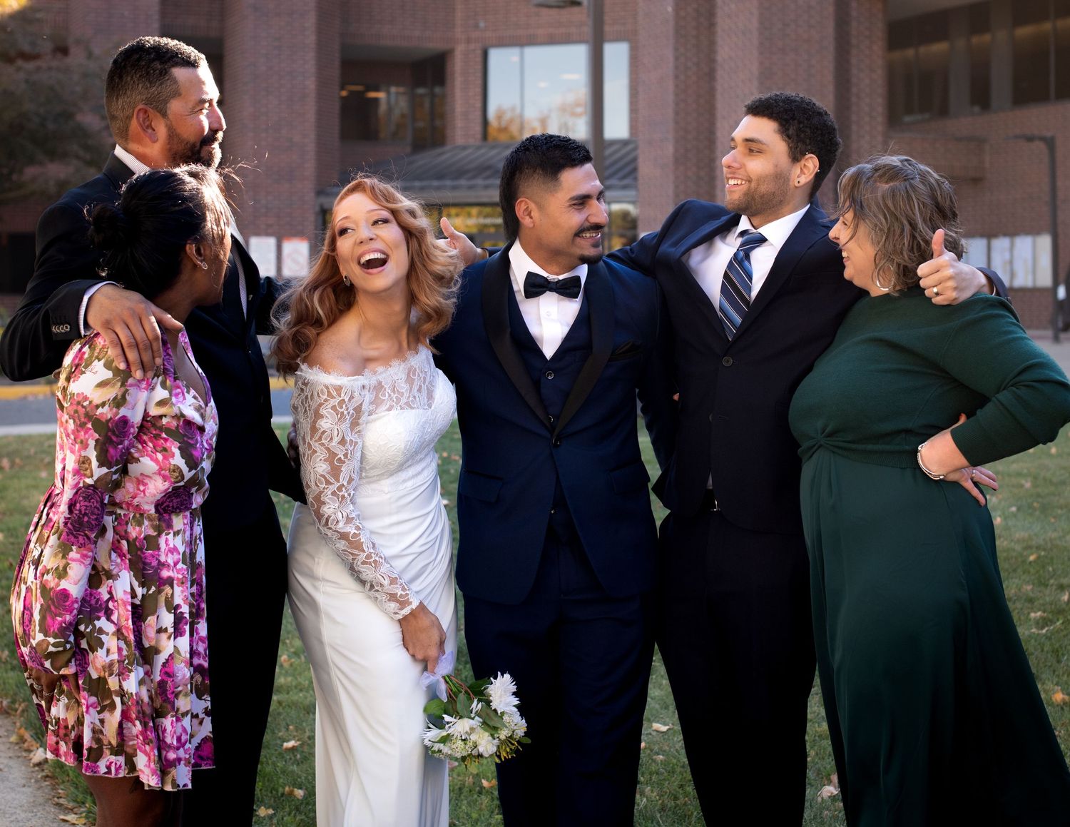 Wedding party of six smiling and celebrating outdoors in formal attire with bride and groom.
